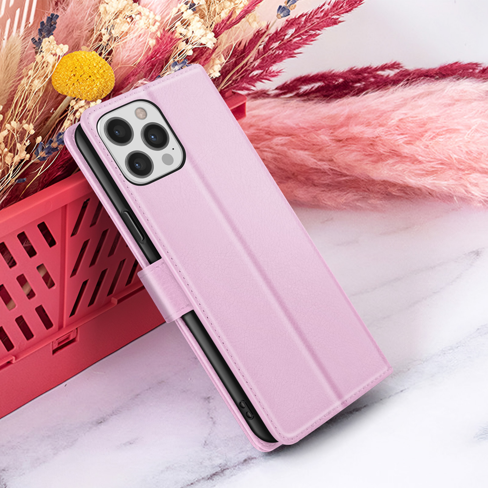 Una custodia rosa per telefono con telefono all'interno, accanto a un cestino rosso e fiori rosa.