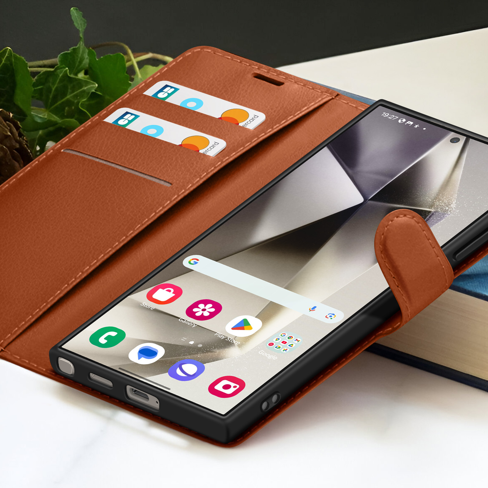 Een smartphone in een bruine leren hoes staat open en toont apps. Creditcards zitten in een zak. Achtergrond met boeken.