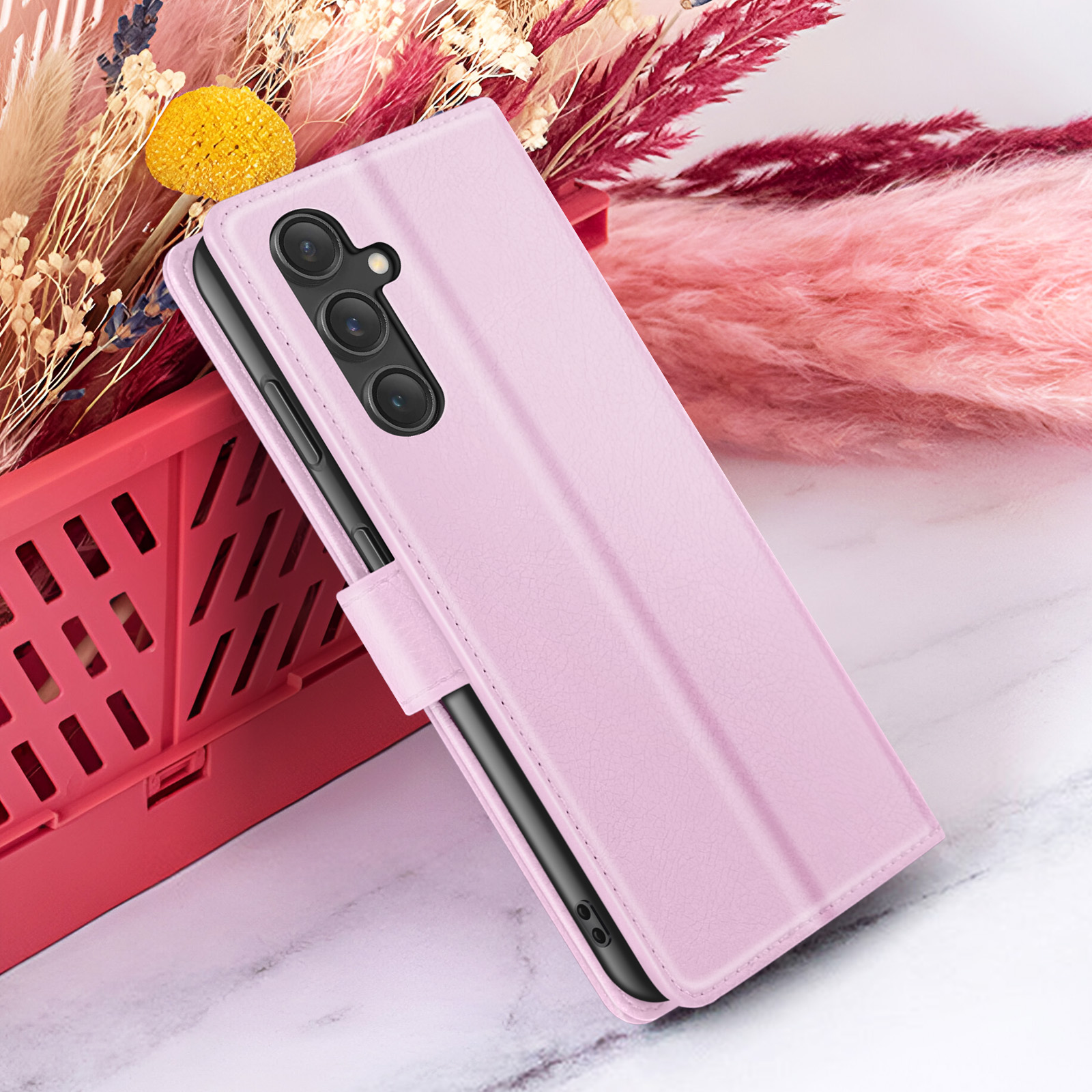Roze telefoonhoesje met telefoon, voor een rode mand met bloemen op een marmeren oppervlak.