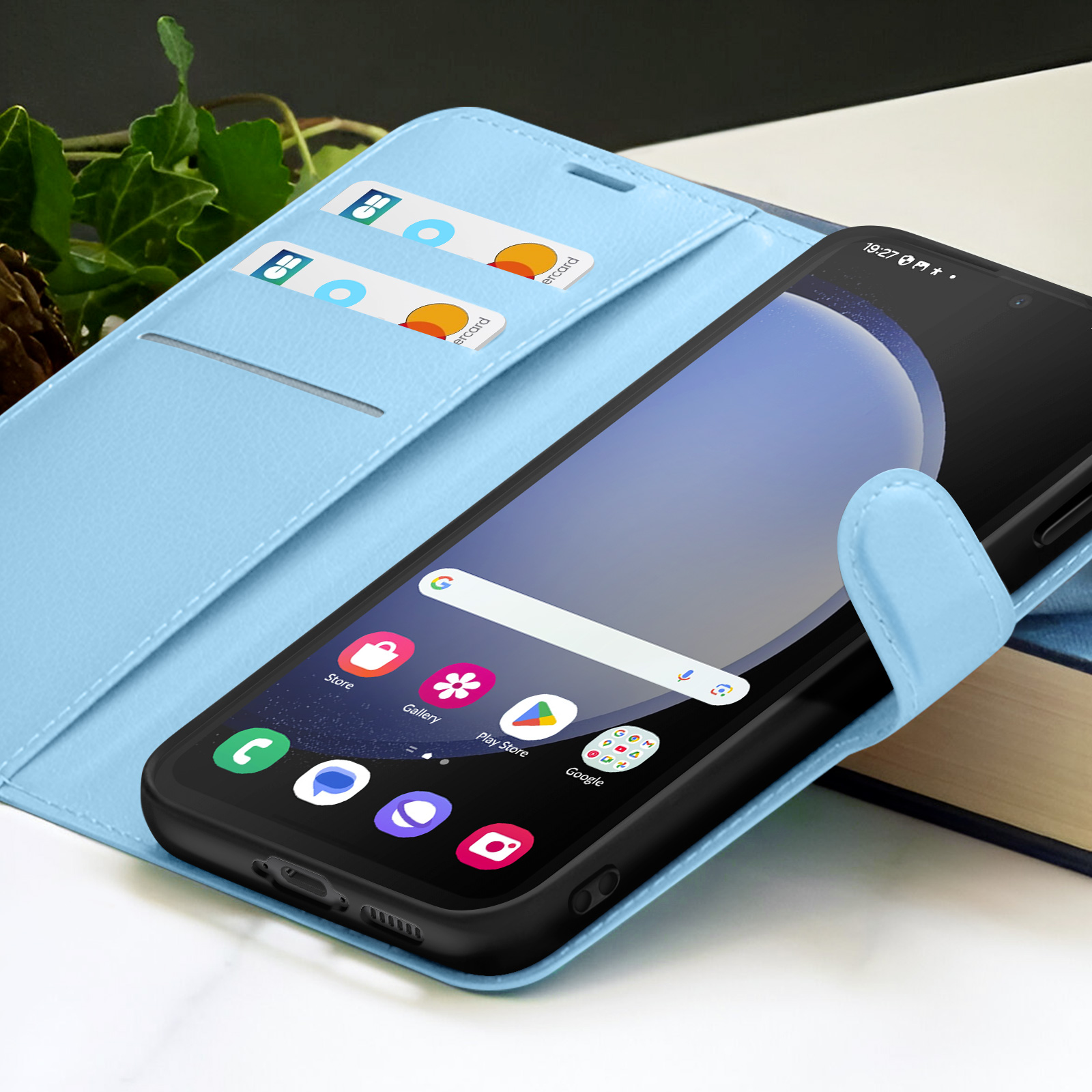 Een smartphone in een lichtblauwe case met creditcards, met app-iconen op het scherm. Achtergrond omvat een boek en bladeren.