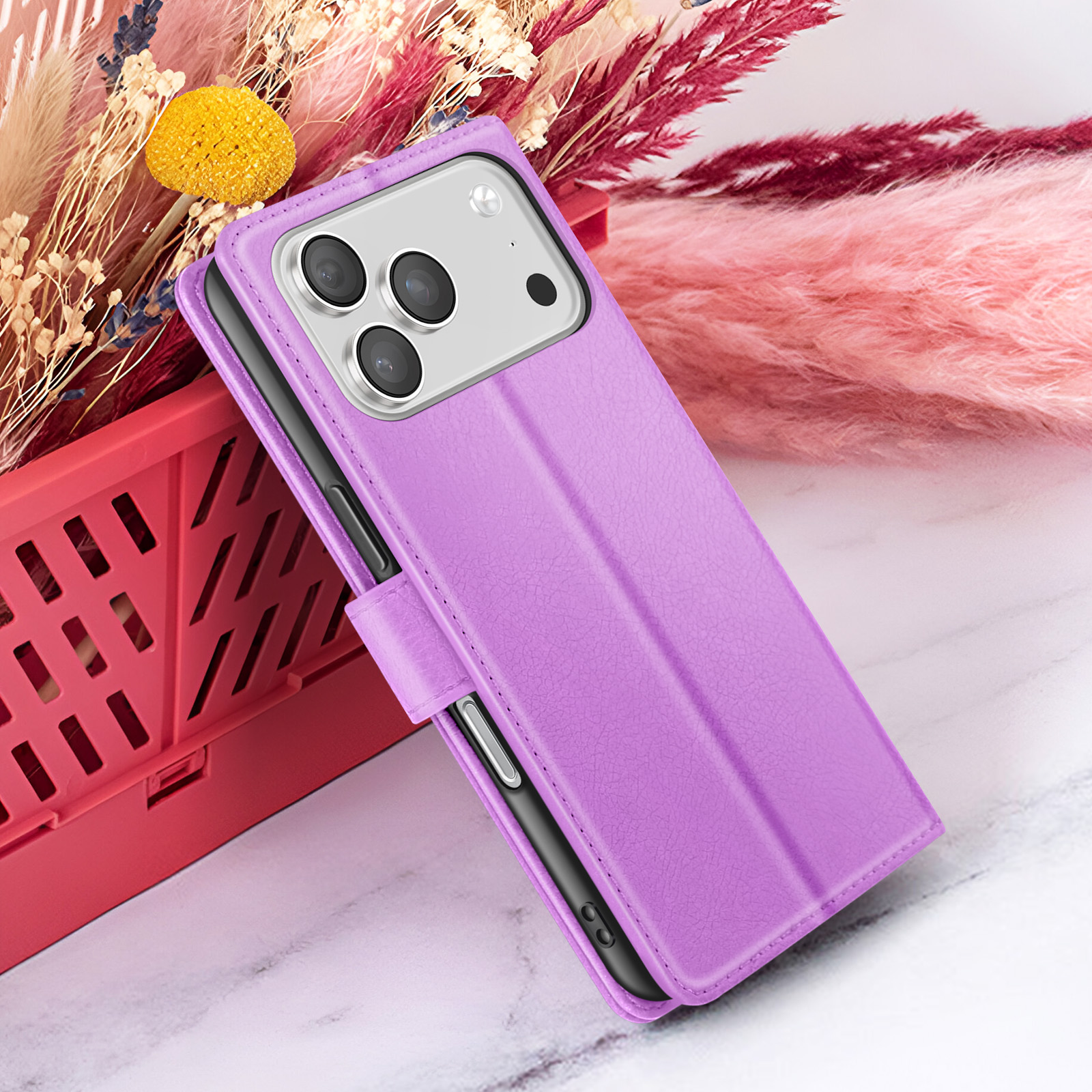 Un étui de téléphone violet avec un téléphone à l'intérieur, posé sur un conteneur rouge avec un fond de fleurs séchées.
