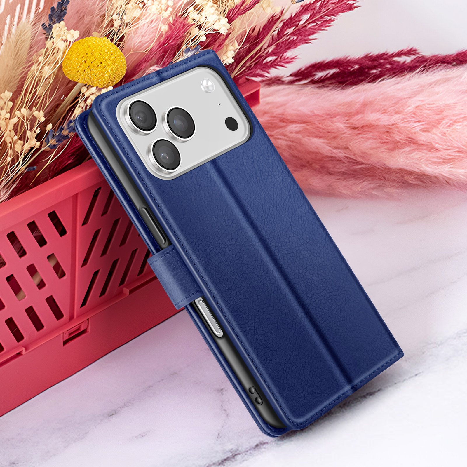 Blauwe leren telefoonhoes met meerdere camera's, liggend op een rode mand met bloemen op de achtergrond.