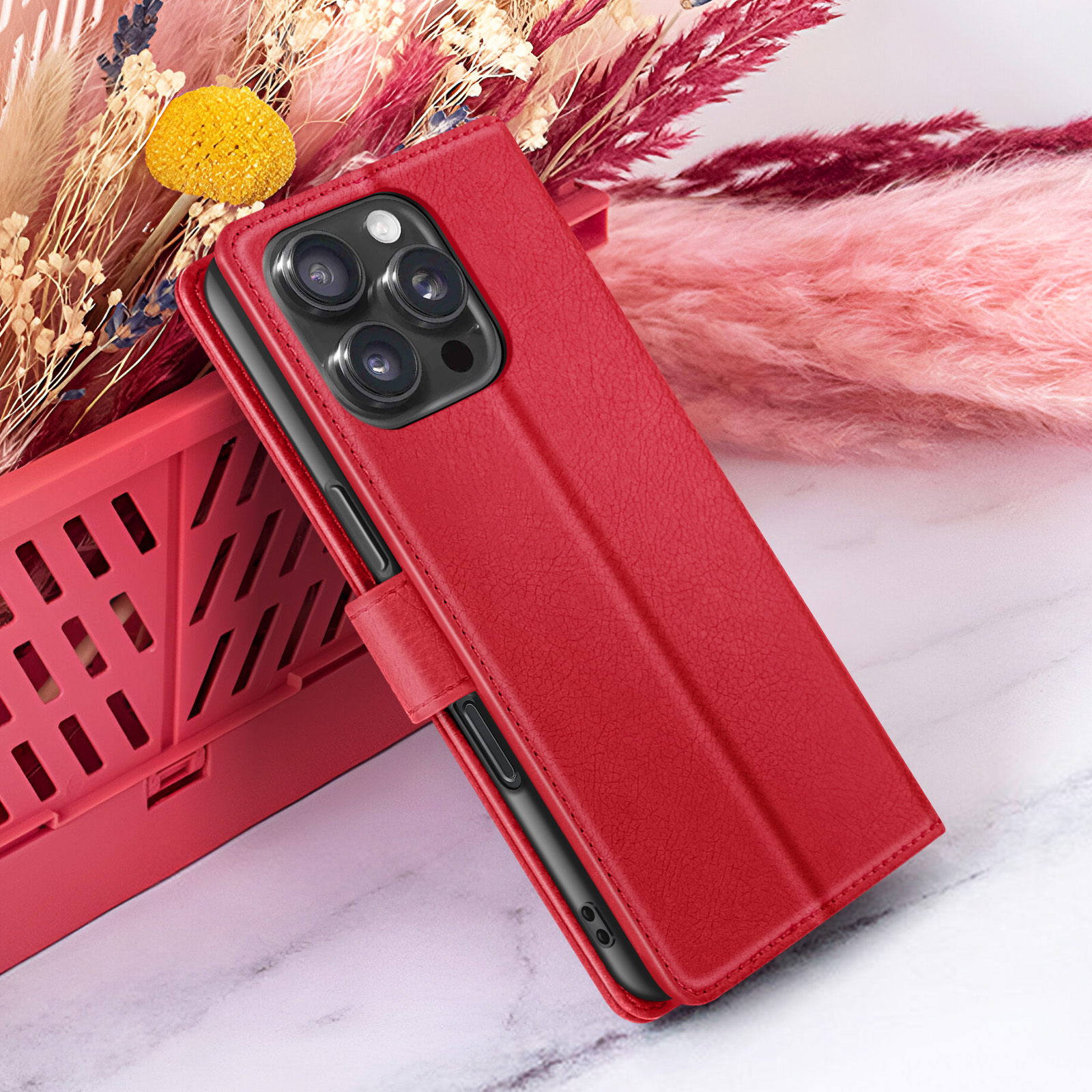 Een rode telefoonhoes met camera ligt op een rode mand. Droogbloemen op de achtergrond.