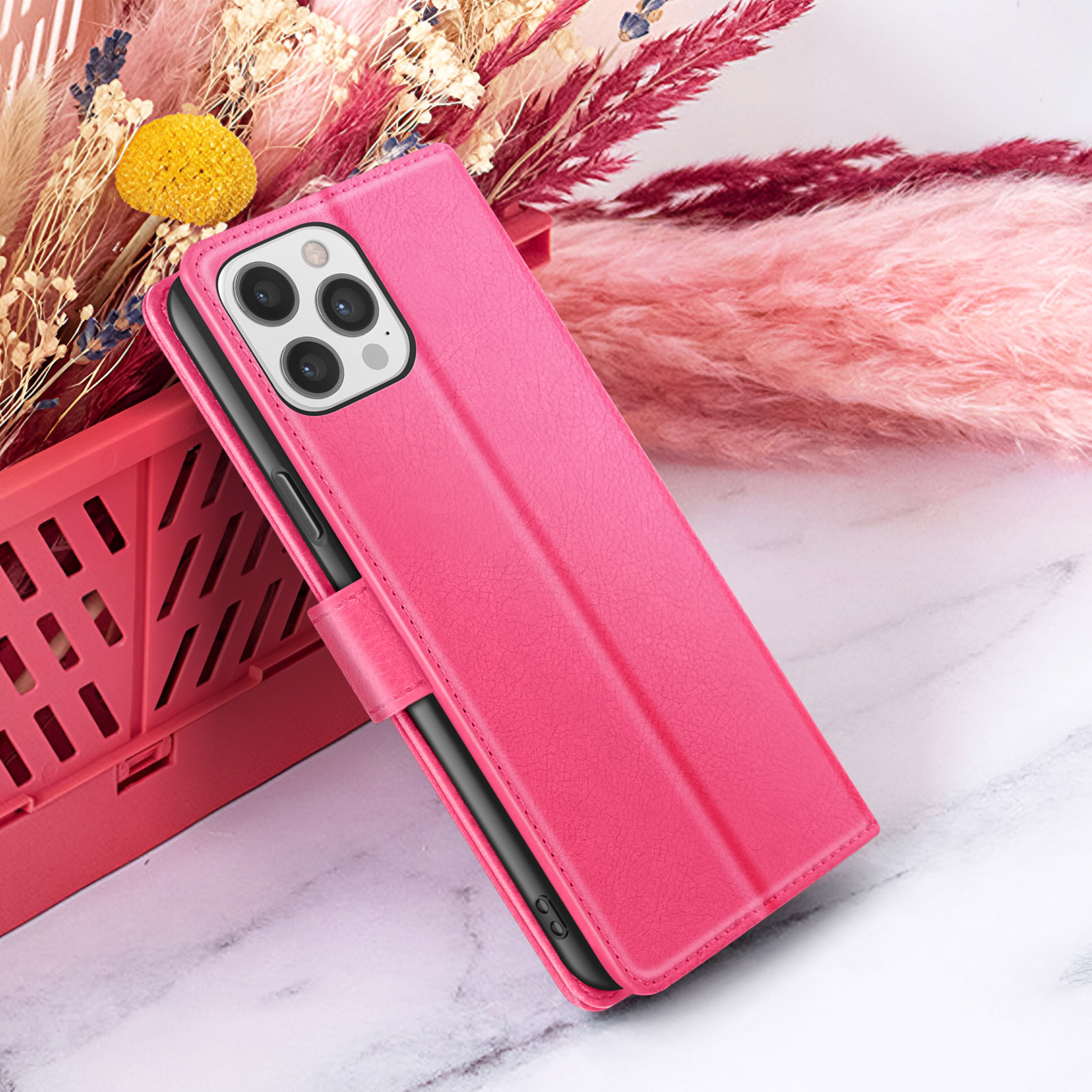 Custodia rosa con telefono all'interno, accanto a un cestino rosa di fiori secchi e uno sfondo rosa e soffice.