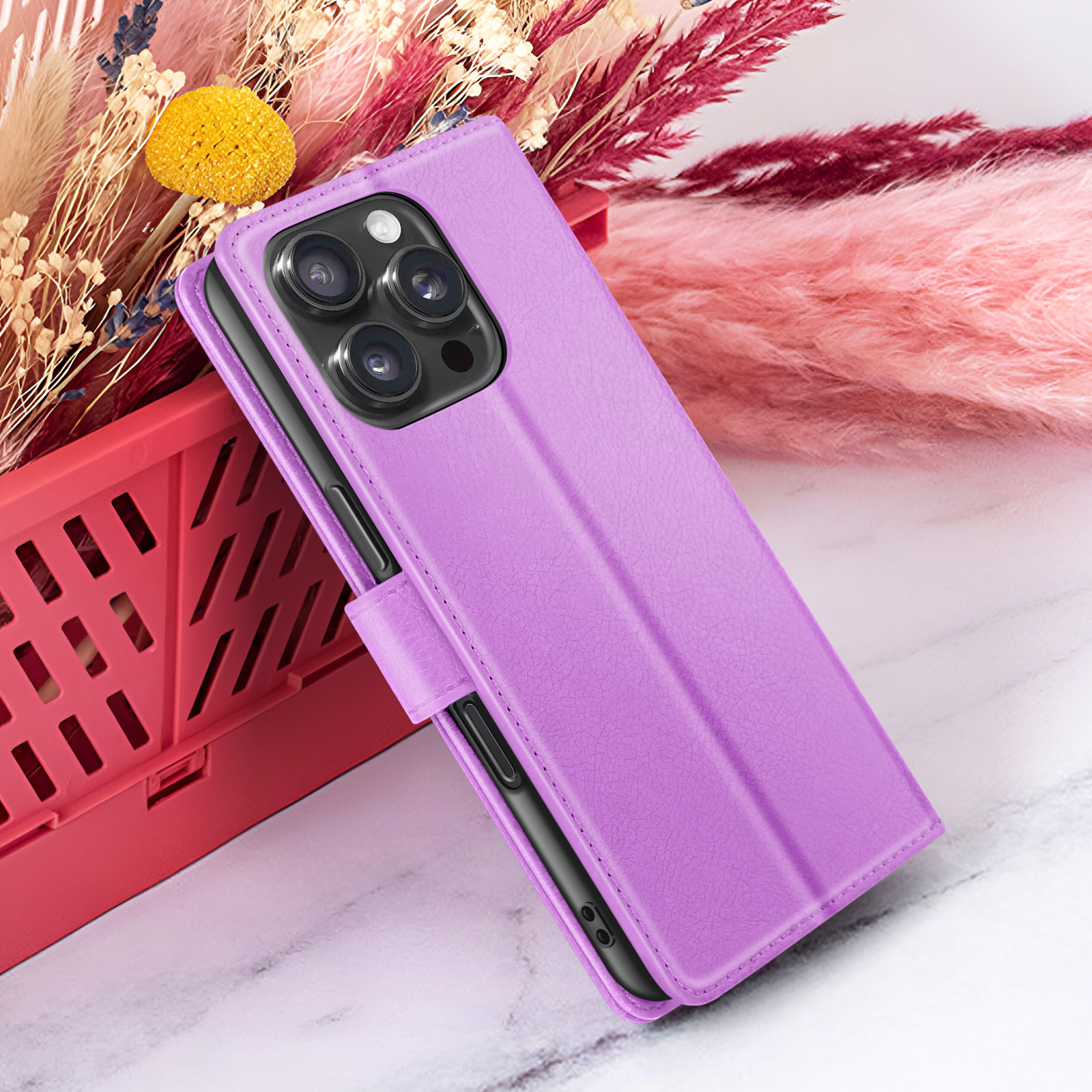 Een paarse telefoonhoes met een telefoon erin staat omhoog. Bloemen en een rode mand op de achtergrond.