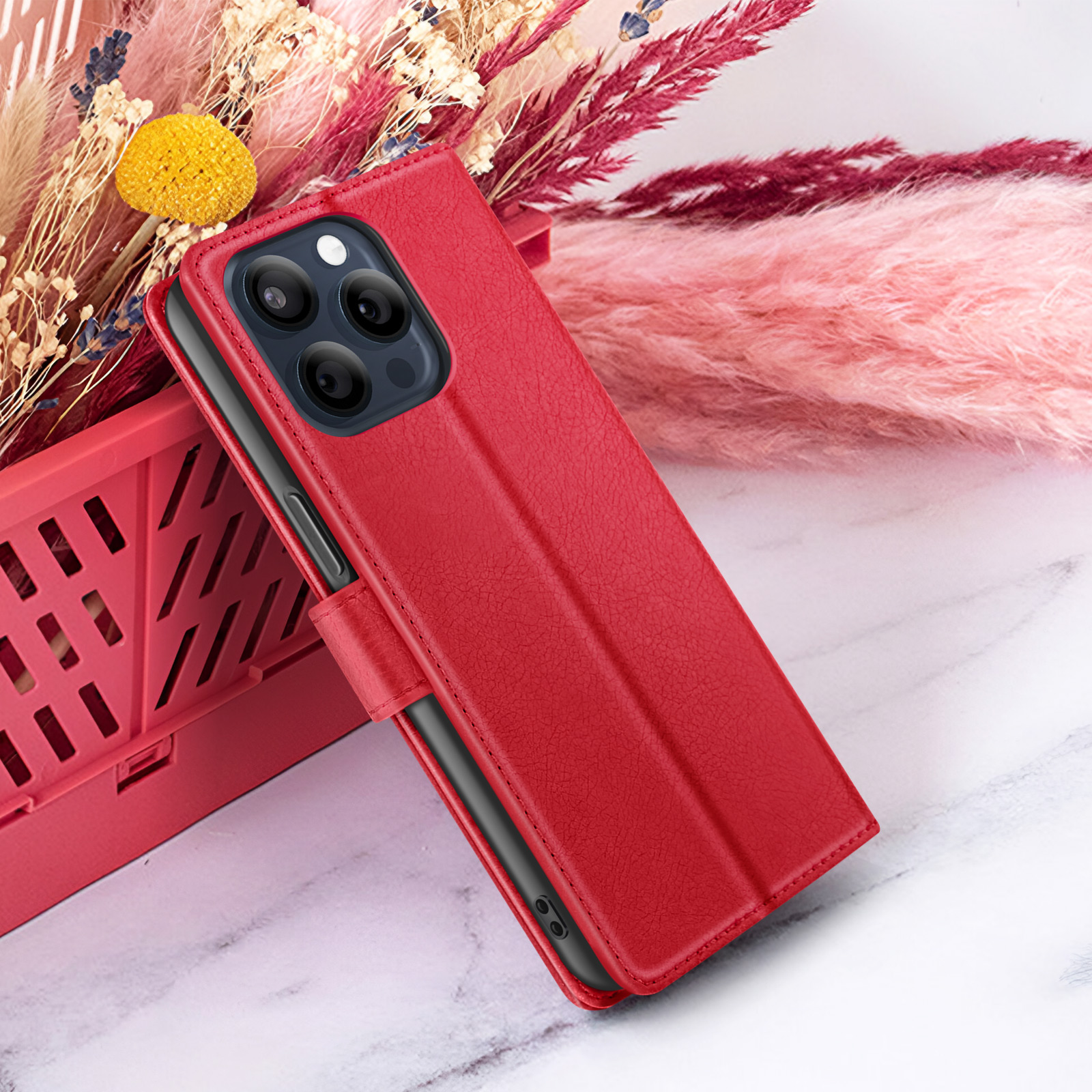 Custodia rossa per telefono con telefono nero all'interno. Dietro un cestino rosso e fiori. Lo sfondo è una superficie di marmo bianco.