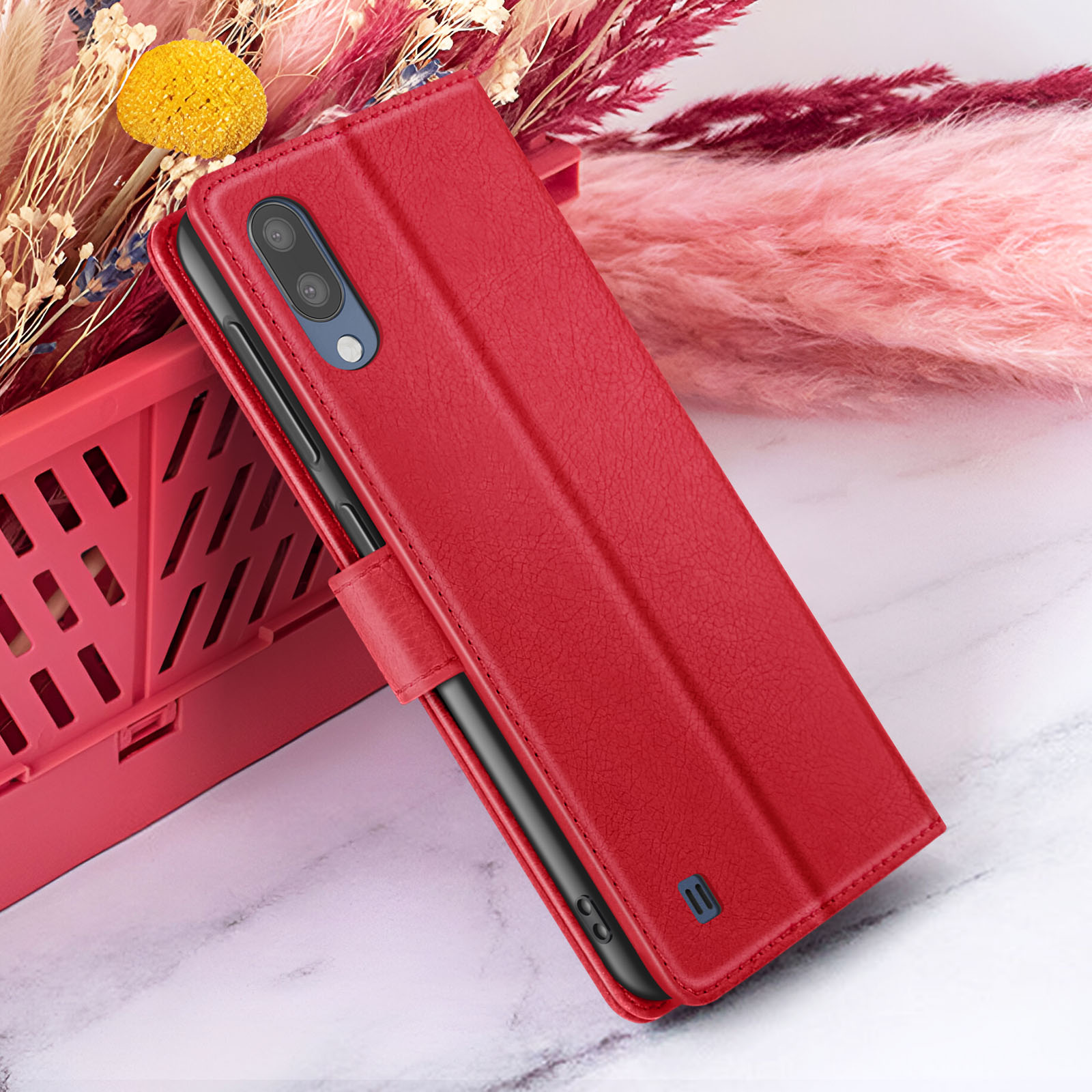 Étui de téléphone rouge avec un téléphone à l'intérieur, à côté d'un panier rouge et de fleurs roses sur marbre.