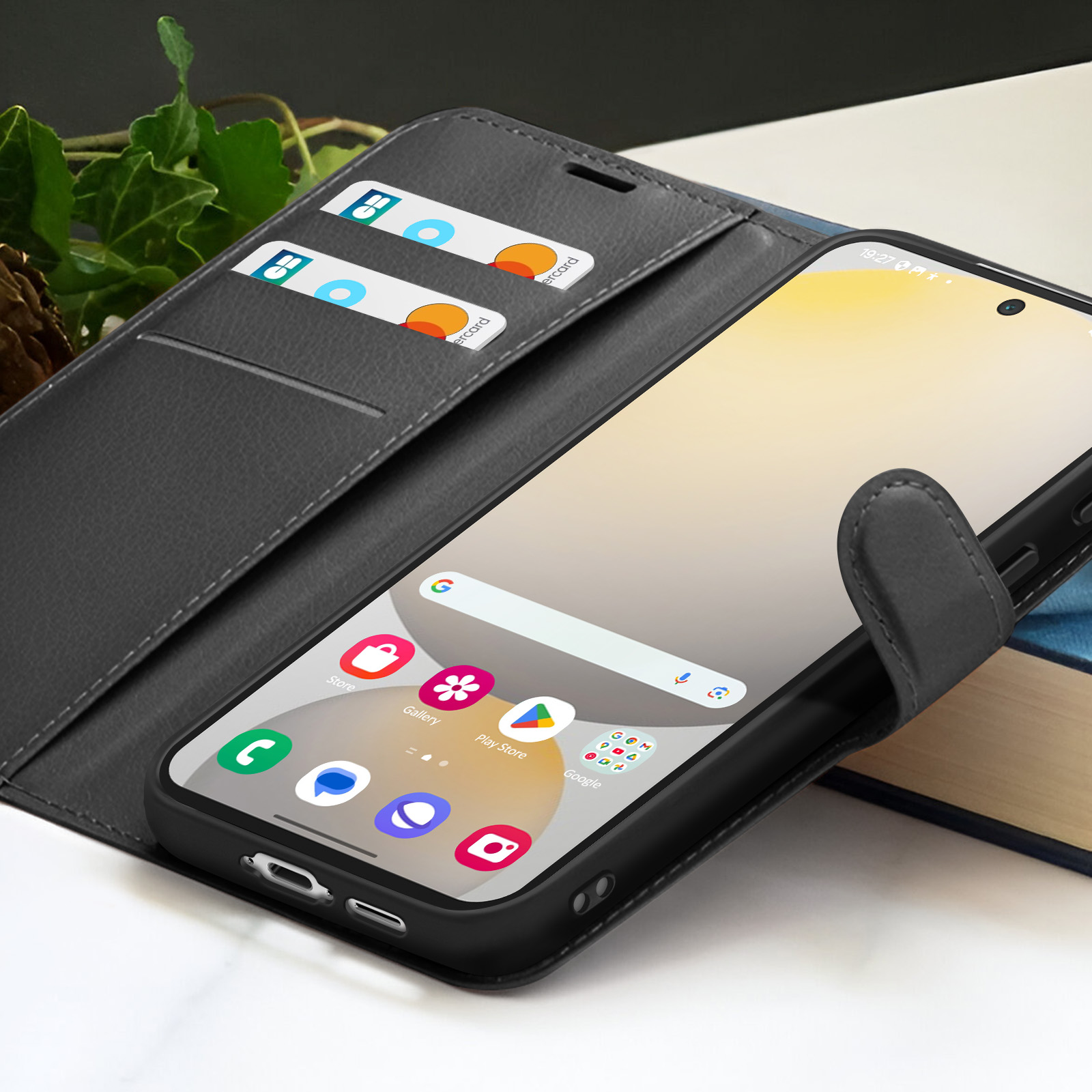 Un smartphone dans un étui noir est ouvert, affichant des applications. L'étui a des fentes pour cartes. Les cartes sont visibles. L'arrière-plan comprend un livre et des plantes.