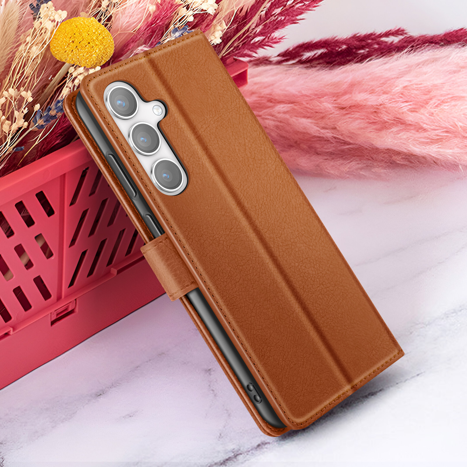Un étui de téléphone en cuir marron sur une surface en marbre, avec des fleurs roses et rouges en arrière-plan.