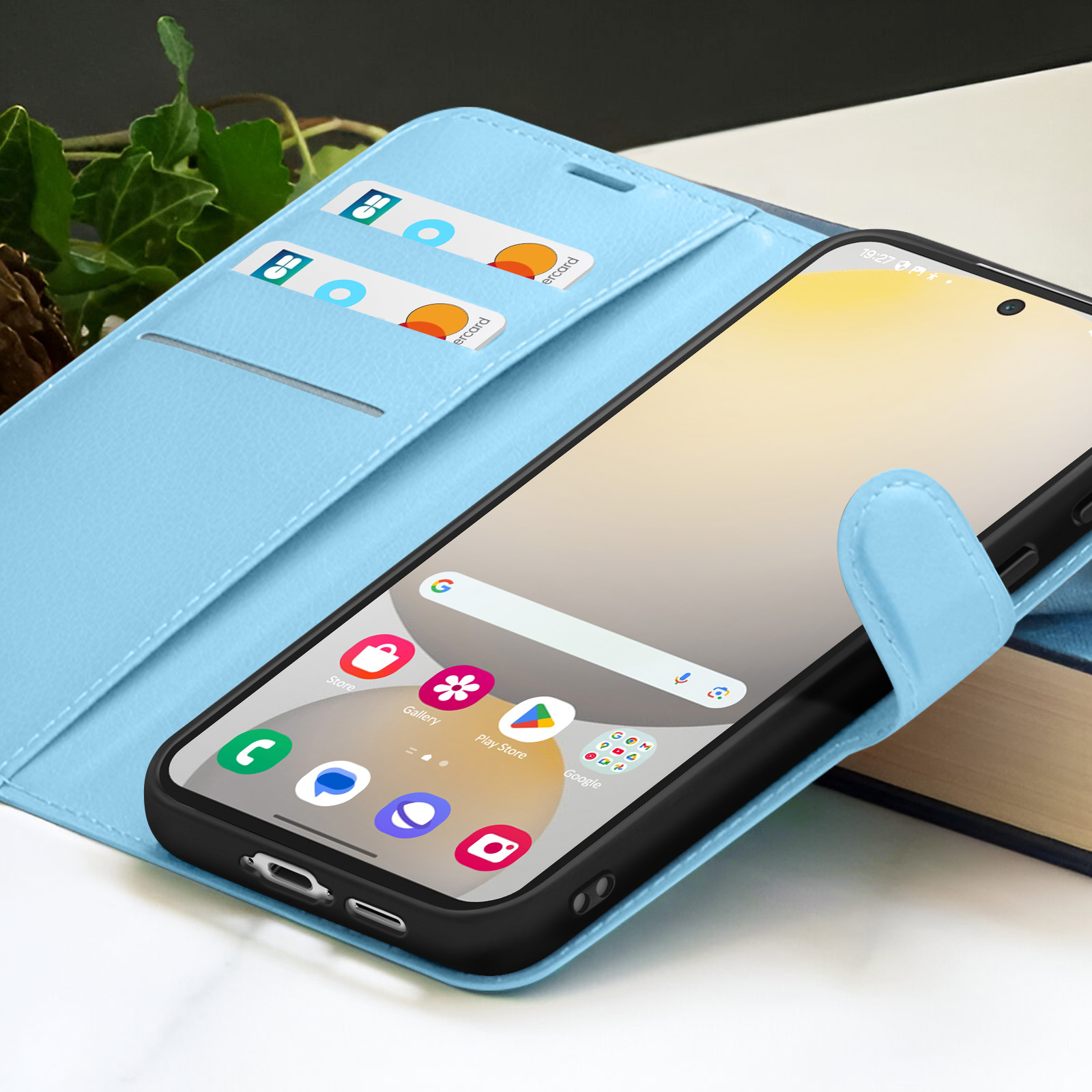 Een smartphone in een lichtblauwe hoes, met kaarten in de hoes en een boek op de achtergrond.