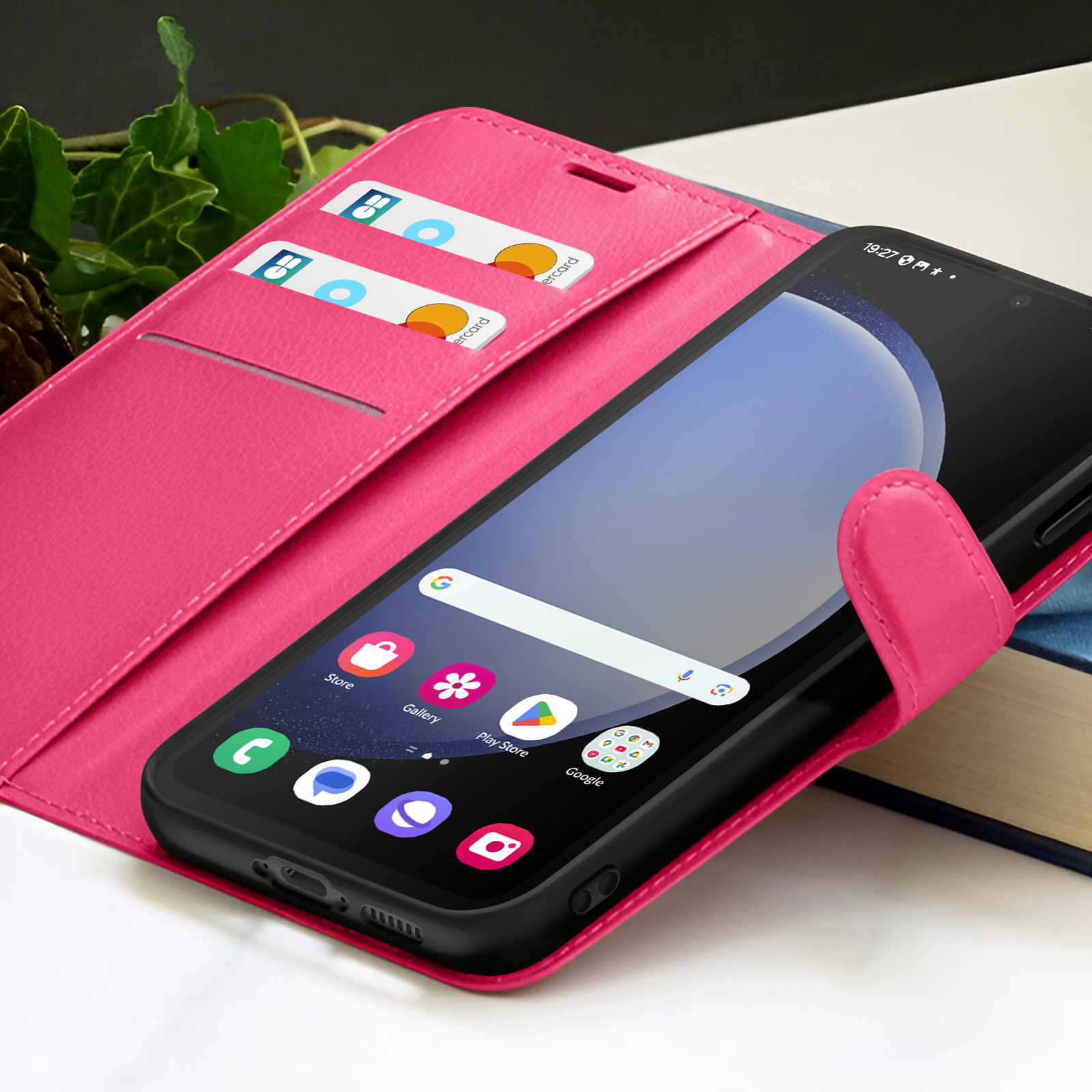 Un smartphone dans un étui rose est ouvert, affichant des applications. Cartes de crédit dans les fentes. Un livre en arrière-plan.
