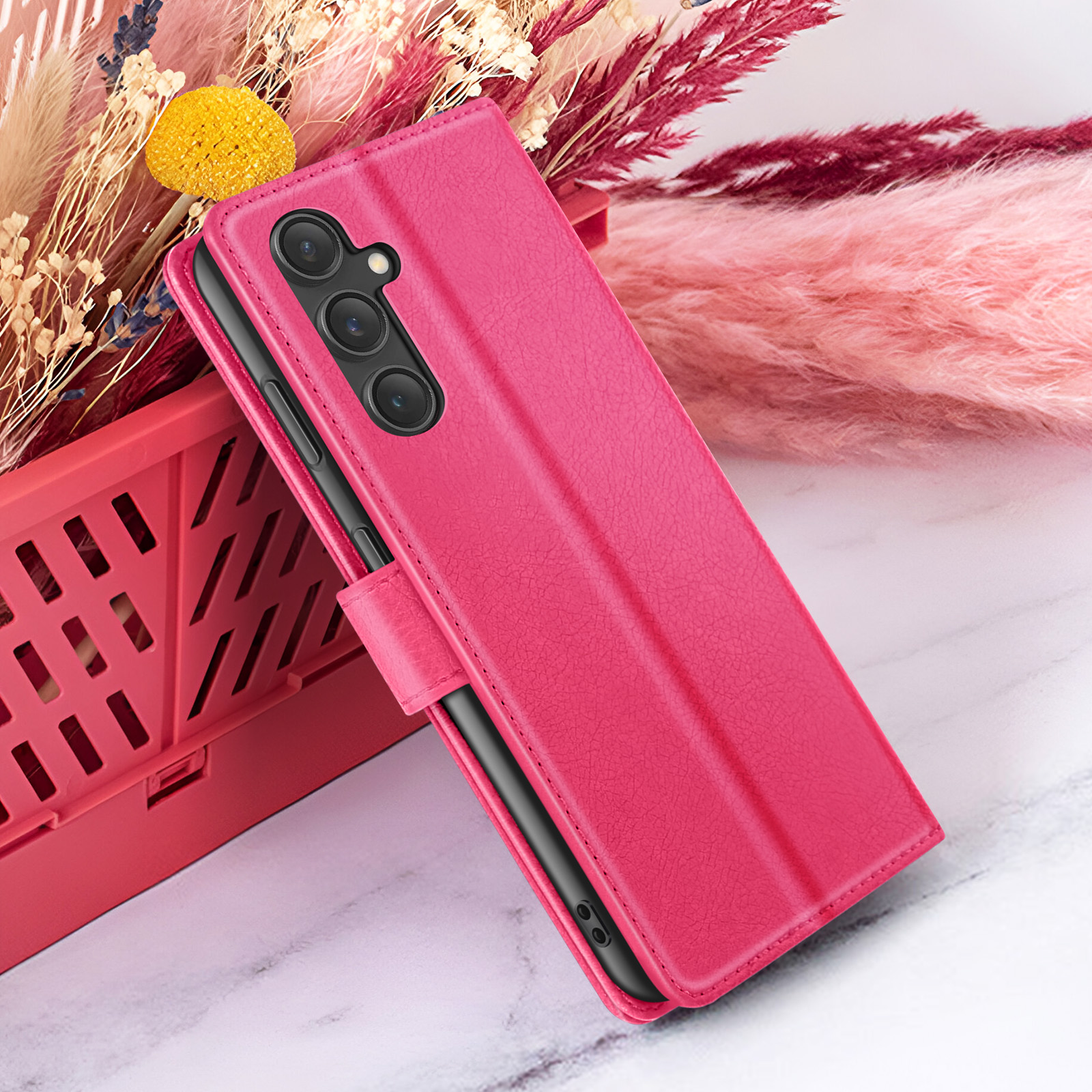 Un étui de téléphone rose avec une caméra est sur une caisse rouge, avec des fleurs séchées en arrière-plan. L'étui est ouvert.
