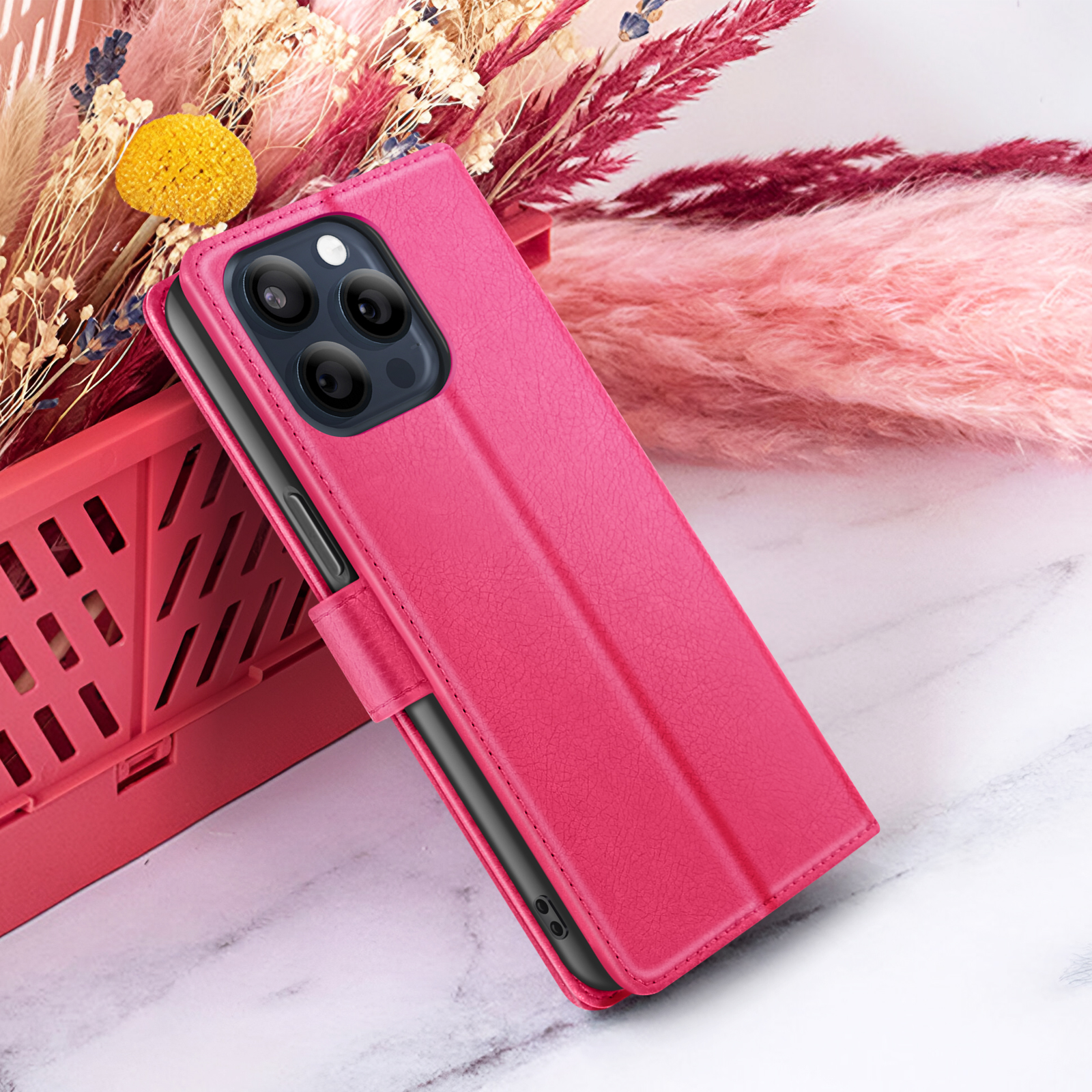 Een roze telefoonhoesje met een zwarte telefoon erin. Achtergrond heeft bloemen en een marmeren oppervlak.