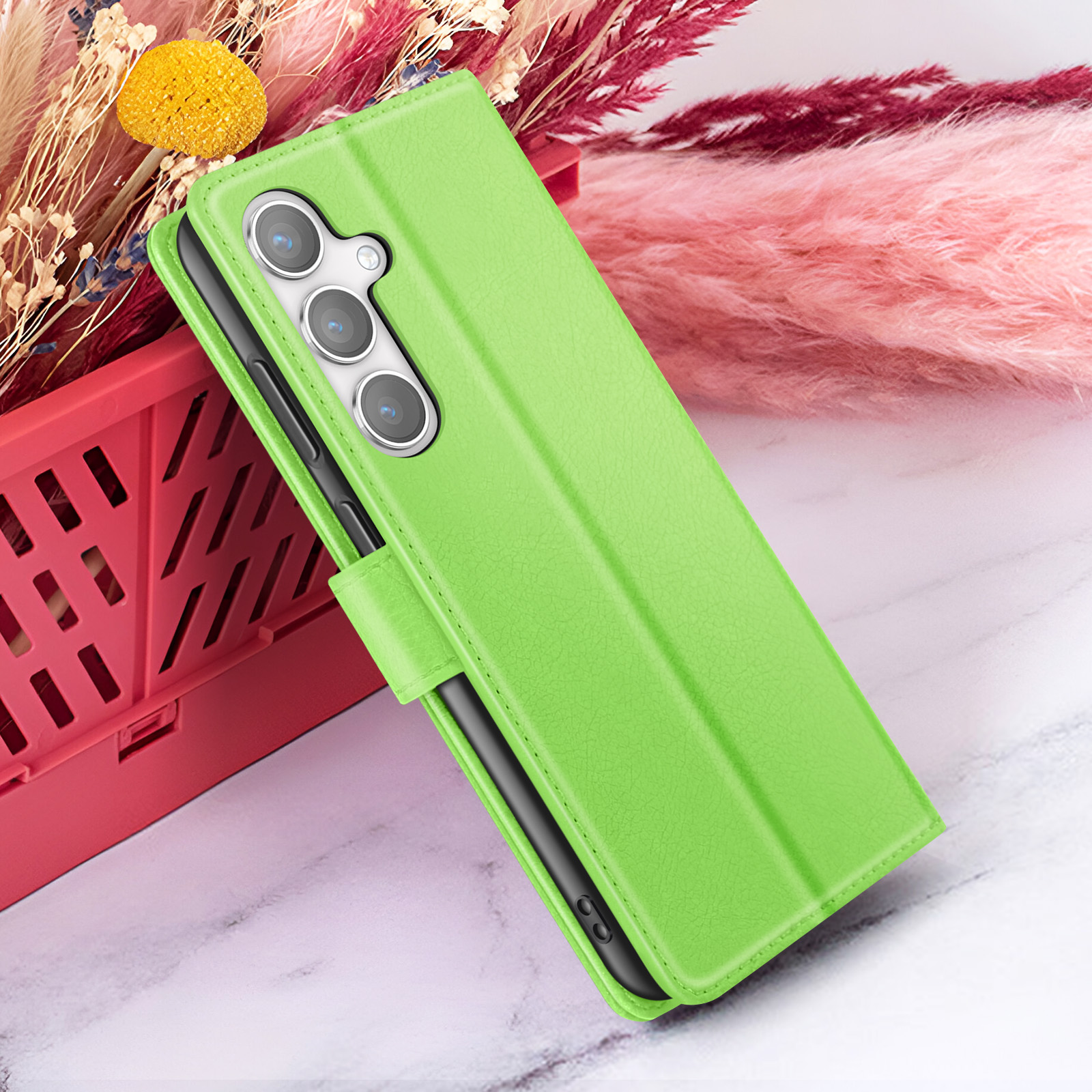 Un étui de téléphone vert avec un téléphone à l'intérieur est posé à côté d'un panier rouge rempli de fleurs décoratives.