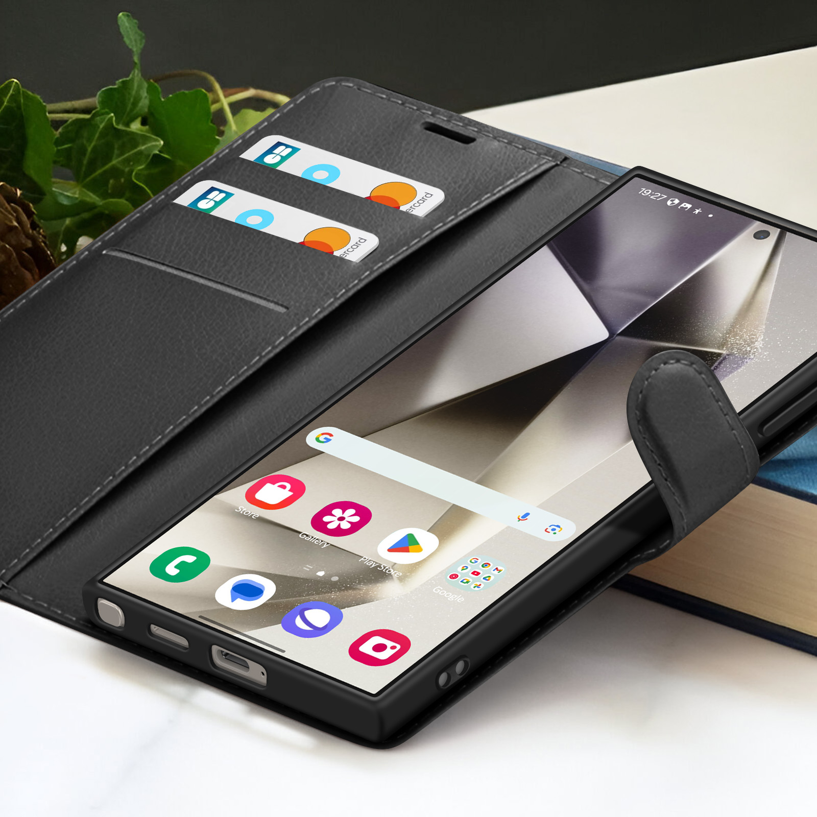 Een smartphone in een zwarte hoes is open en toont het startscherm. Creditcards zijn zichtbaar in de hoes. Achtergrond omvat boeken en bladeren.