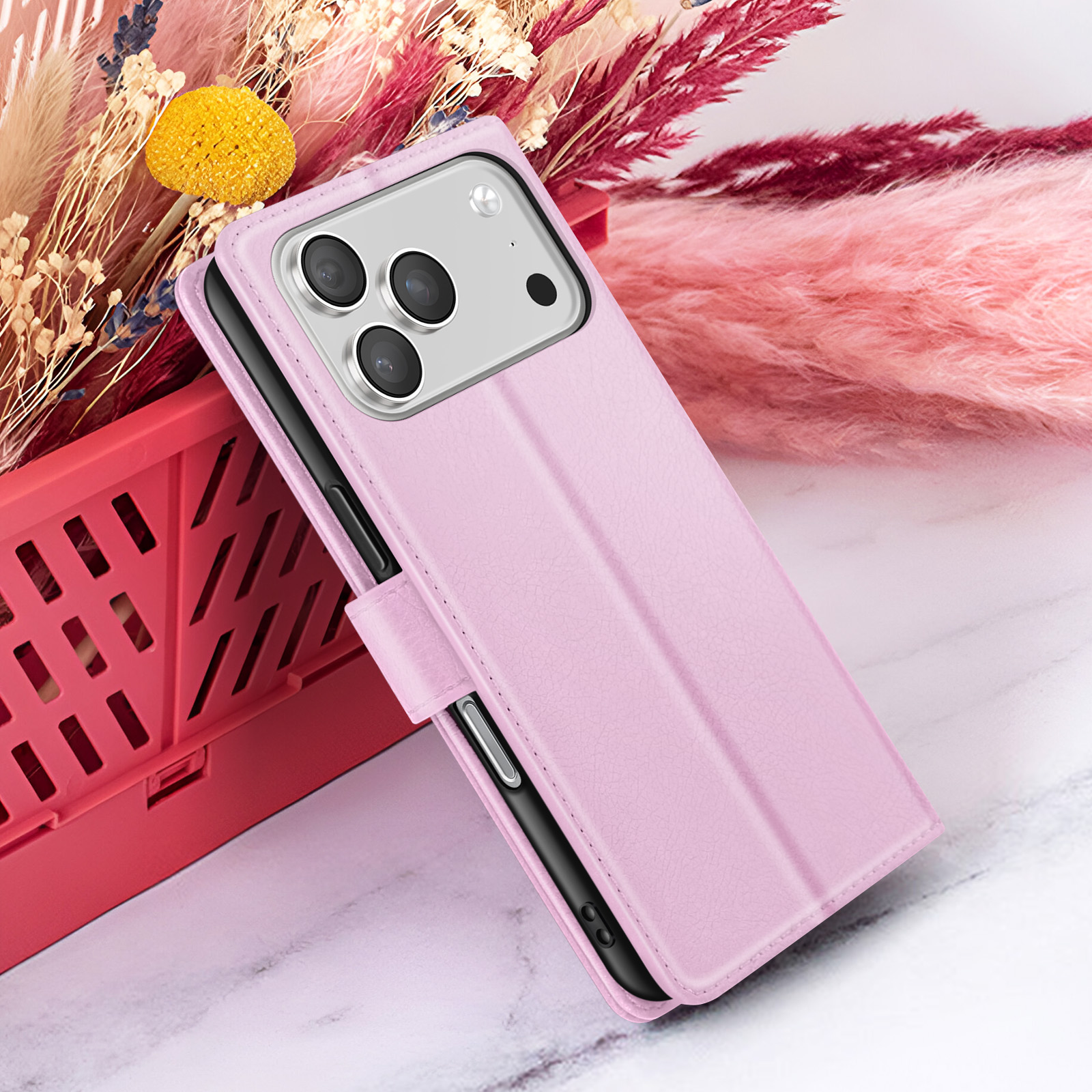 Een roze telefoonhoesje met een telefoon erin, voor een rode mand en een bloemenachtergrond.