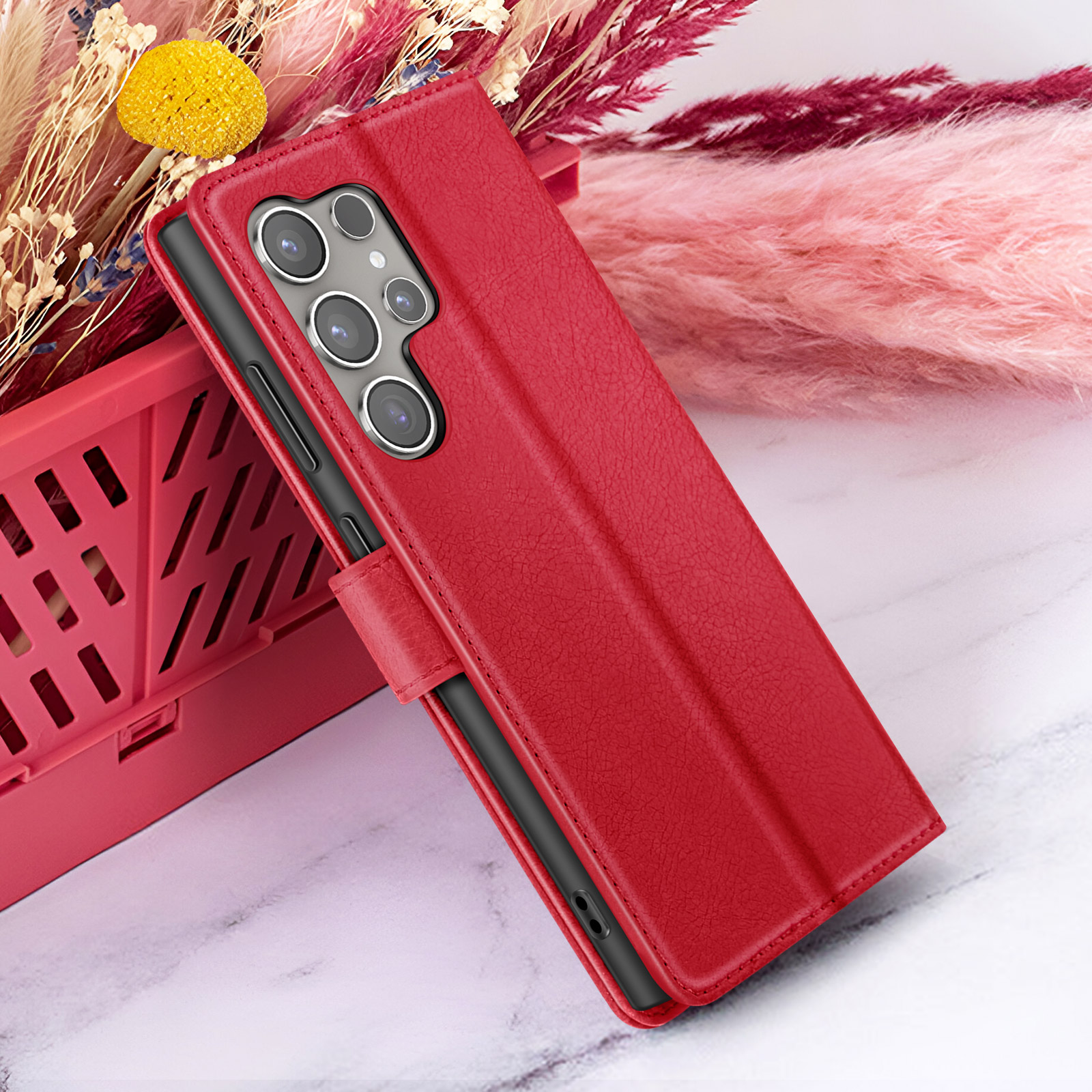 Rode telefoonhoes met meerdere camera's. Het ligt op een marmeren oppervlak met bloemen en een rode mand op de achtergrond.