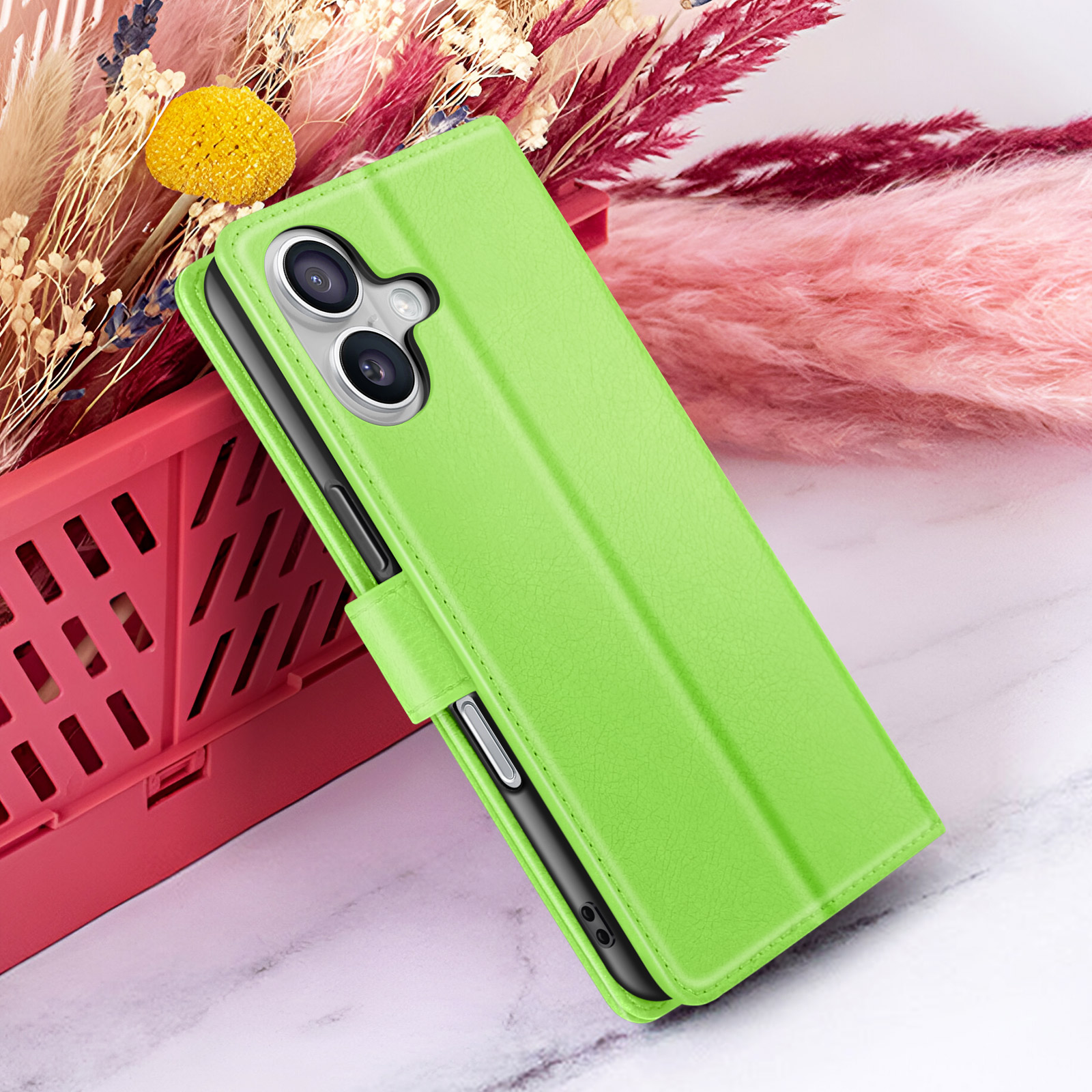 Un étui de téléphone vert avec un téléphone à l'intérieur, placé devant des fleurs séchées et un récipient rouge.