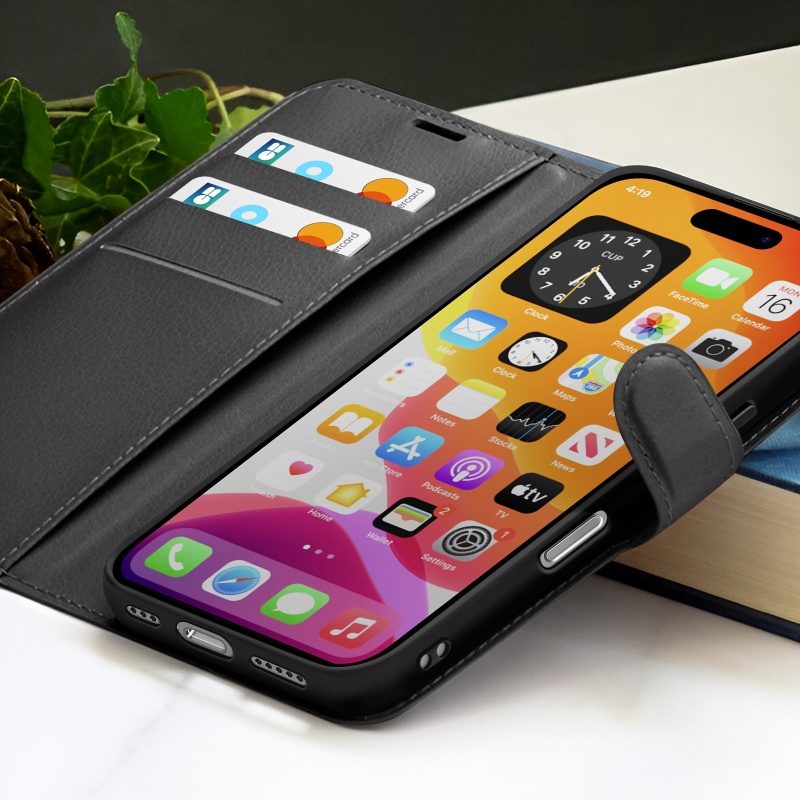 Uno smartphone nero in una custodia a portafoglio mostra le icone delle app. Carte di credito nella custodia. Sfondo con un libro e foglie.