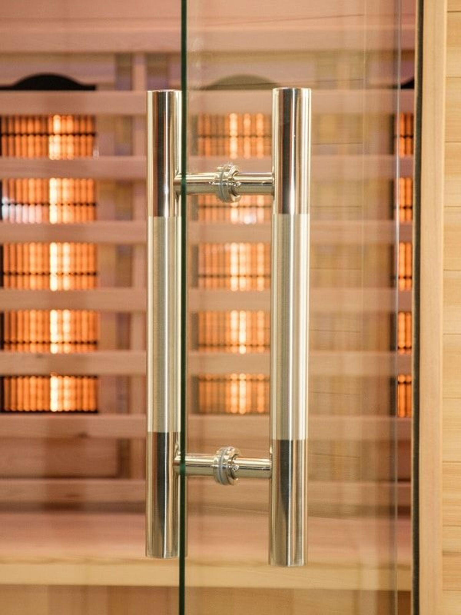 Una puerta de cristal con un tirador metálico. El fondo muestra el interior de una sauna de madera con luces cálidas.