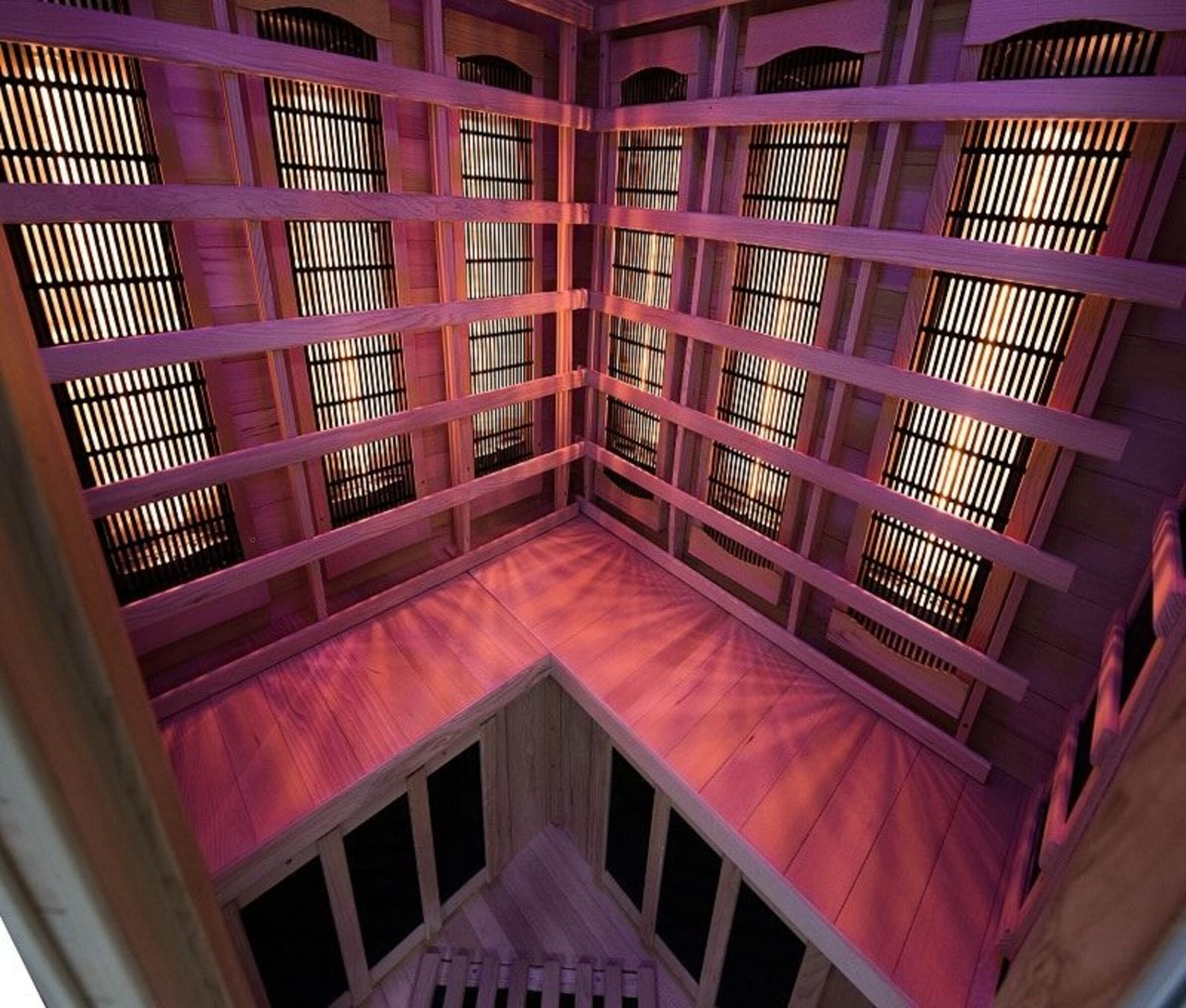 Dentro de una sauna de madera. Se ven listones horizontales y rejillas verticales. El interior está iluminado con un tinte rosado.