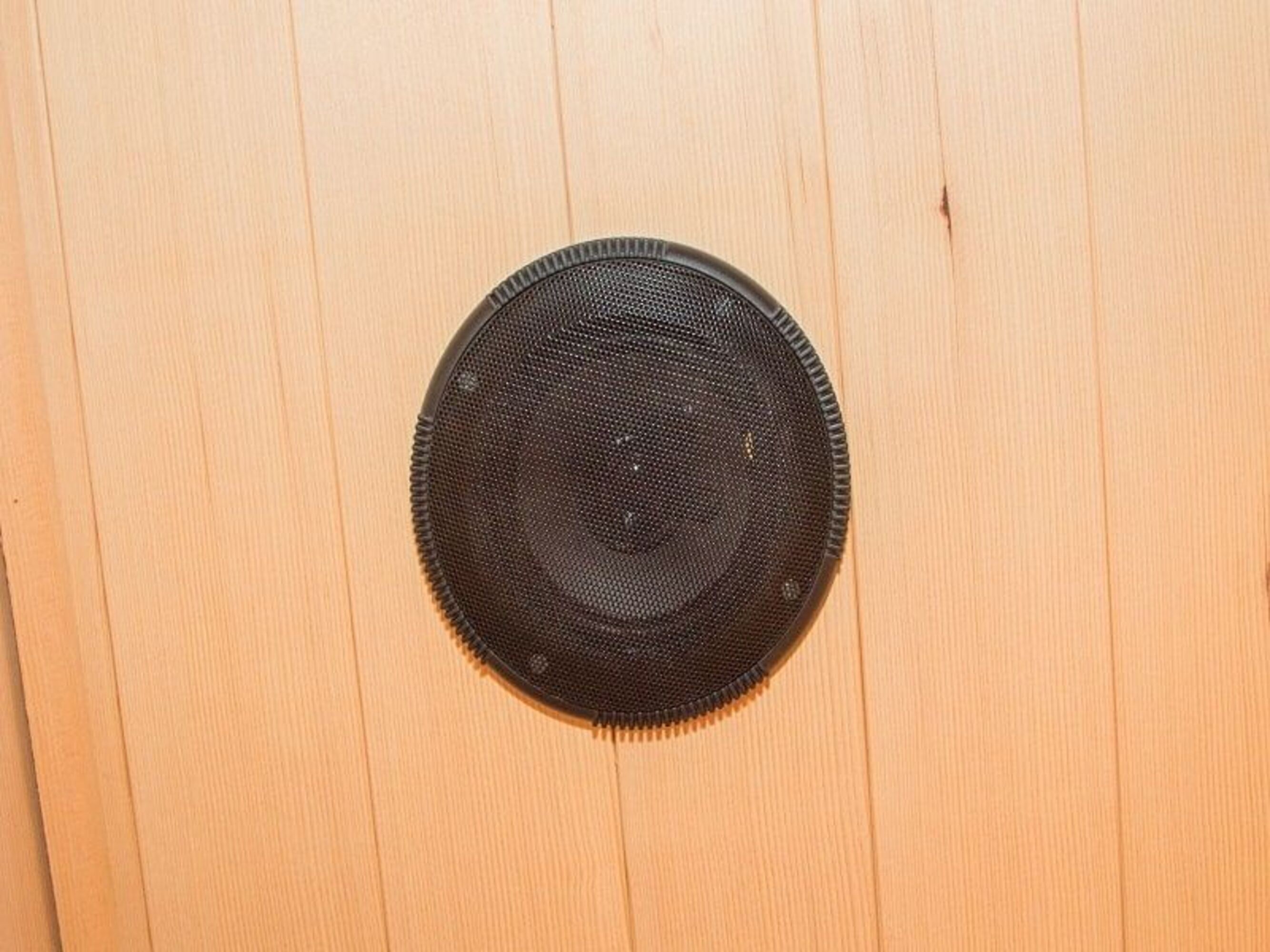 Un altavoz negro montado en un panel de madera clara. El panel es de tablas de madera verticales.