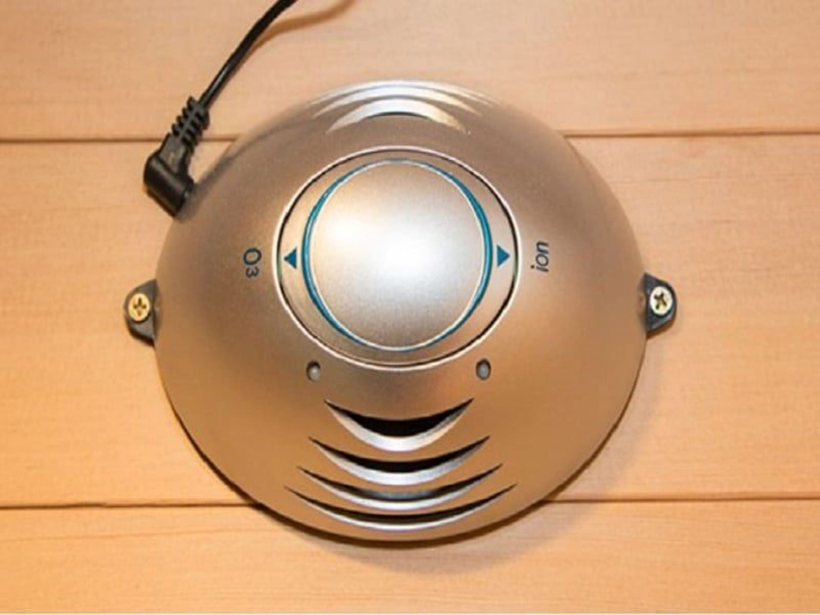 Un generador de ozono e iones plateado sobre una superficie de madera. Tiene un dial de control y un cable de alimentación.