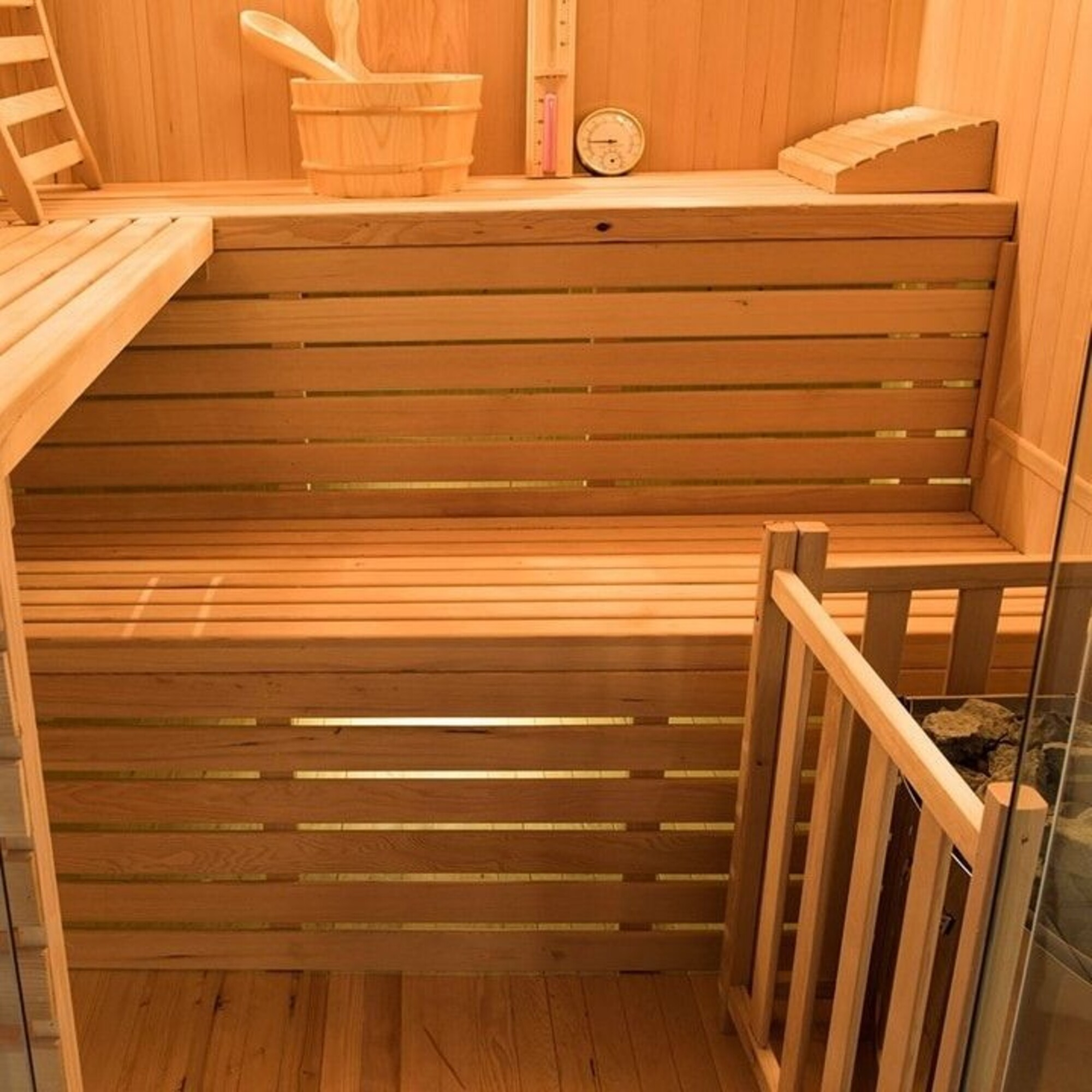 Interior de sauna de madera con bancos, un cubo y un termómetro. La escena es cálida y acogedora, con detalles de madera.