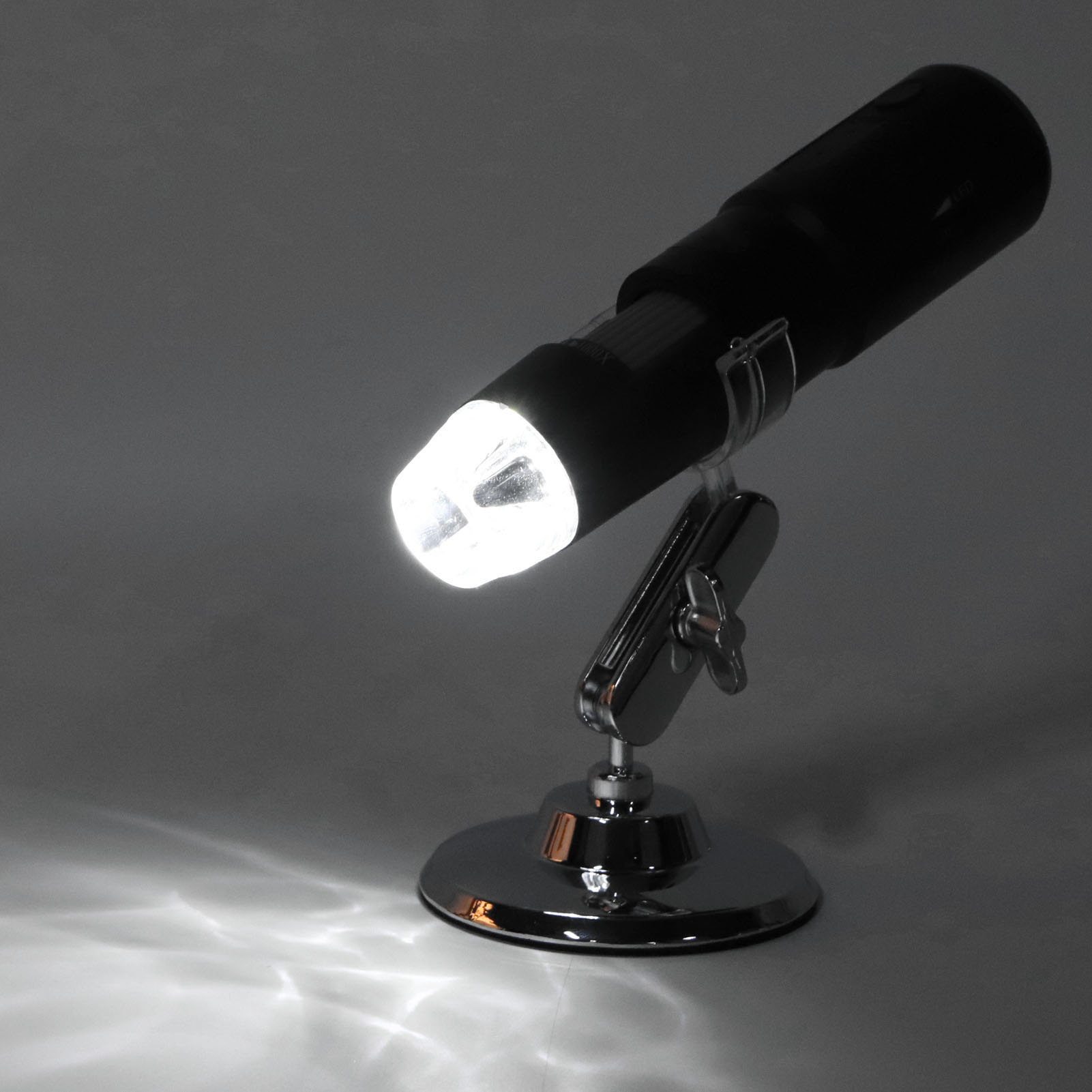 Ein schwarzes Mikroskop mit hellem Licht vor grauem Hintergrund. Das Licht wirft Schatten auf die Oberfläche.