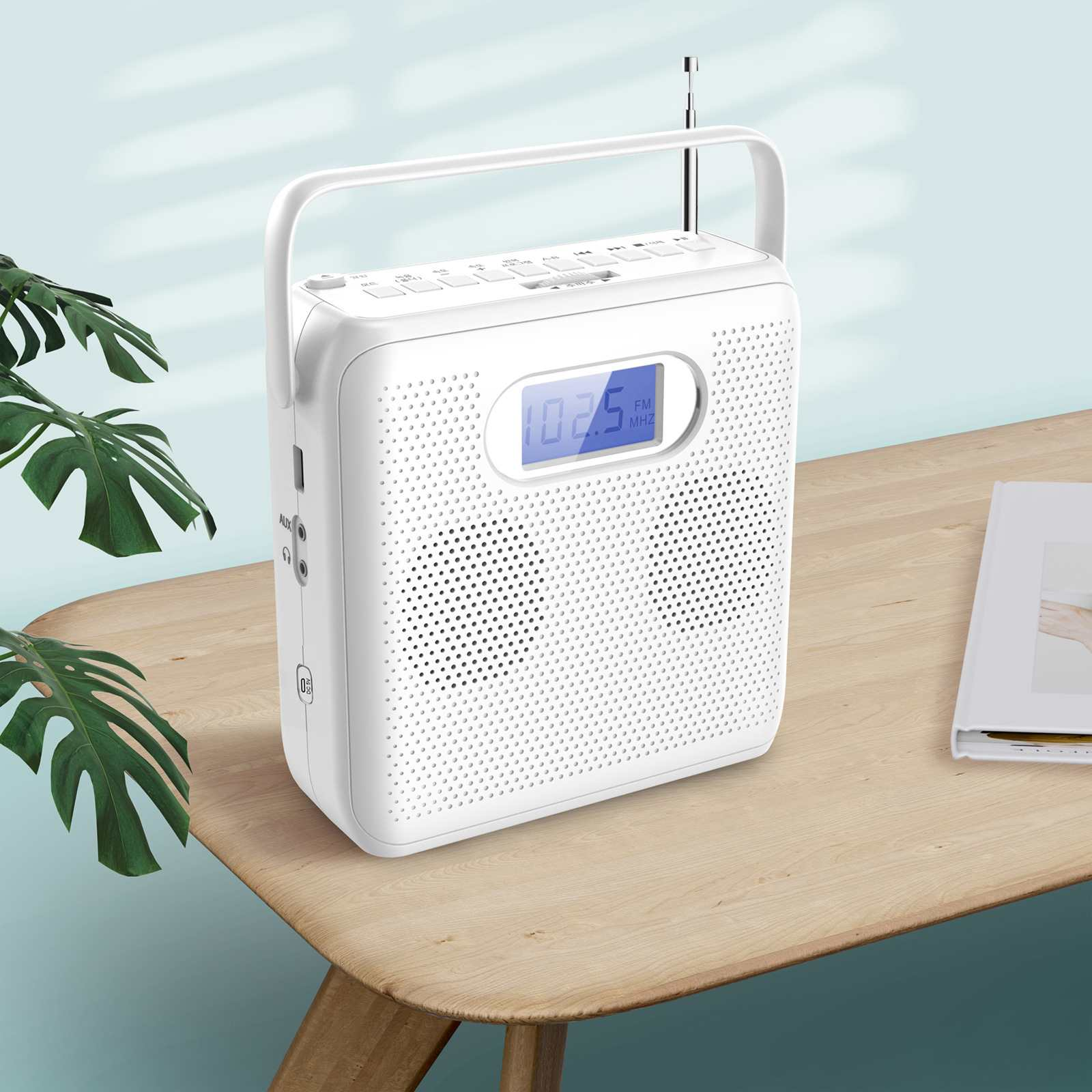 Ein weißes tragbares Radio mit Griff steht auf einem Holztisch. Das Radio zeigt 102,5 FM an. Rechts liegt ein Buch.