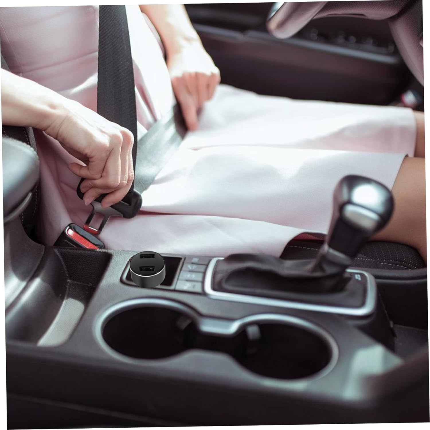 Eine Person im Auto legt den Sicherheitsgurt an. Das Innere des Autos umfasst einen Schalthebel, ein USB-Ladegerät und Getränkehalter.