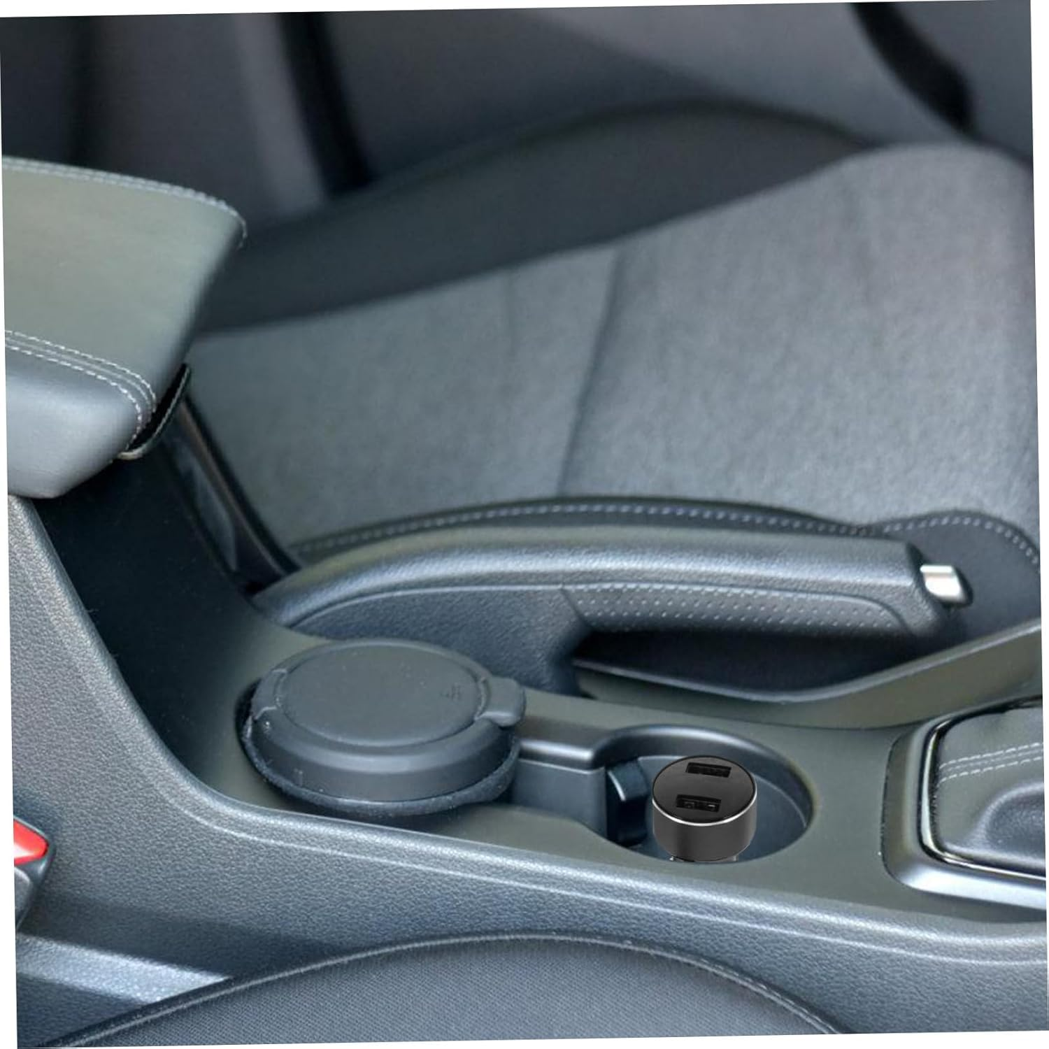 Autoinnenraum mit USB-Ladegerät im Getränkehalter. Schwarze Ledersitze und -verkleidung sind sichtbar. Ein geschlossener Deckel ist ebenfalls vorhanden.