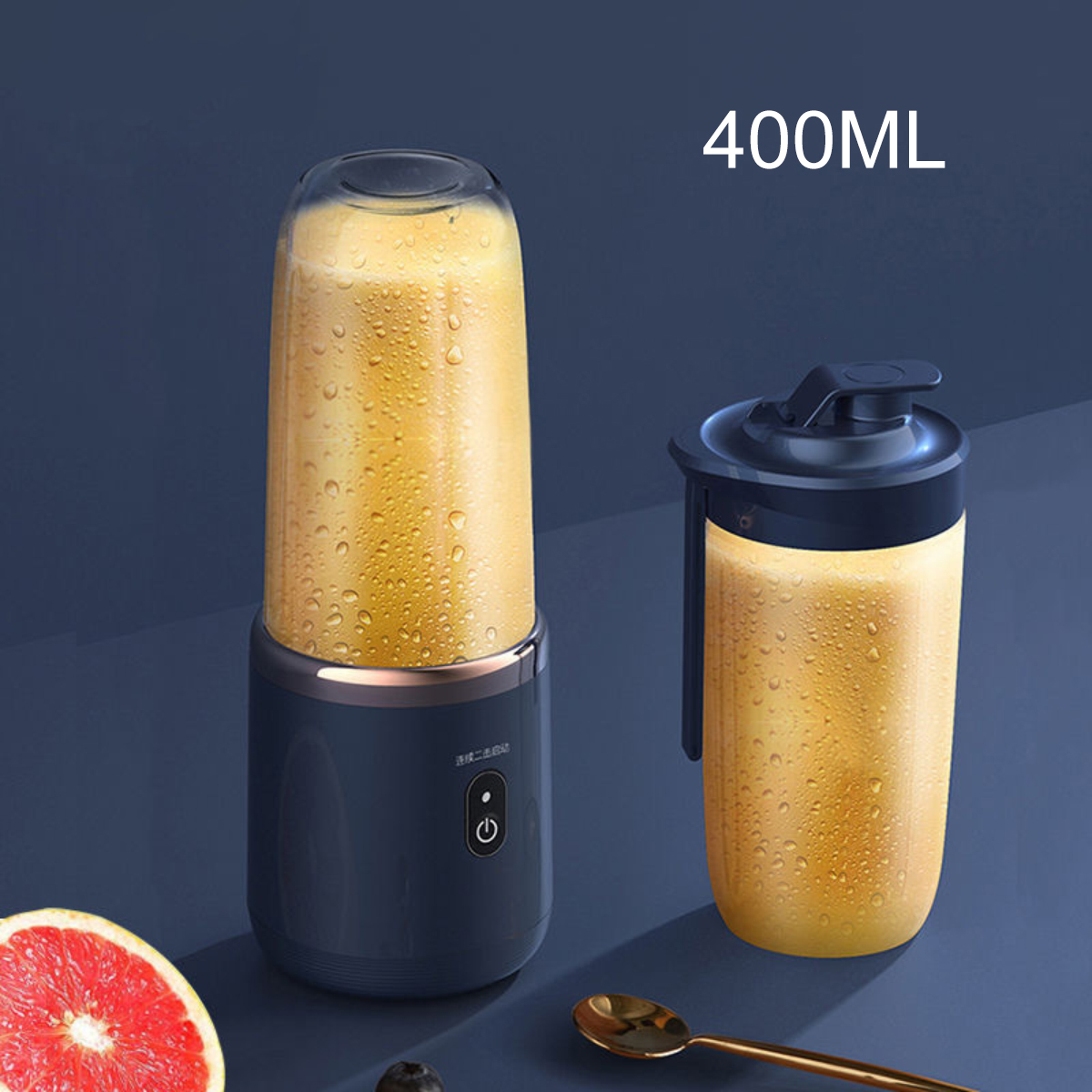 Ein kleiner Mixer mit Saft, eine gefüllte Tasse und ein Löffel auf einer dunkelblauen Oberfläche. Eine Grapefruit-Hälfte ist sichtbar.