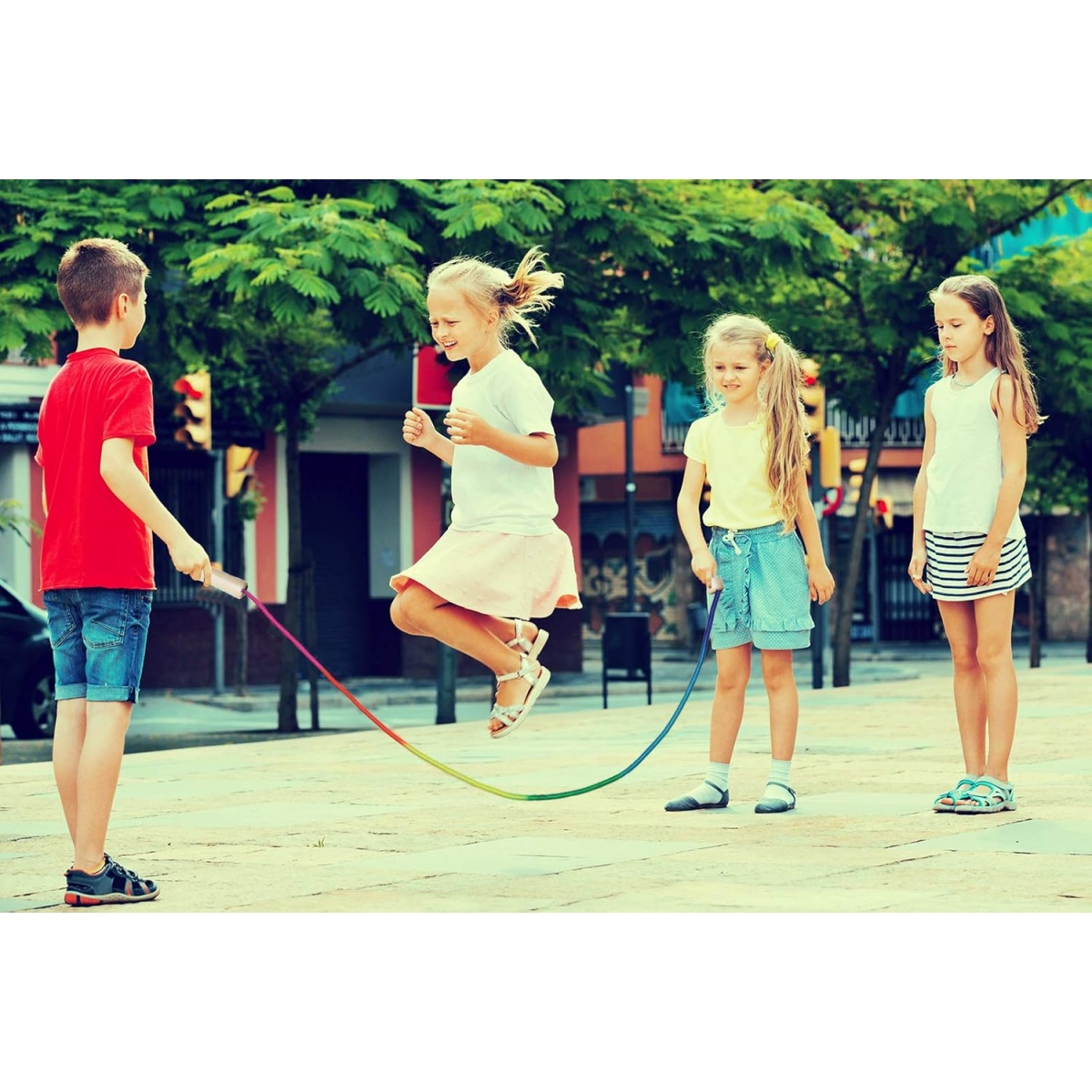 Vier Kinder spielen draußen Seilspringen. Ein Junge hält das Seil. Ein Mädchen springt. Zwei andere Mädchen stehen daneben.