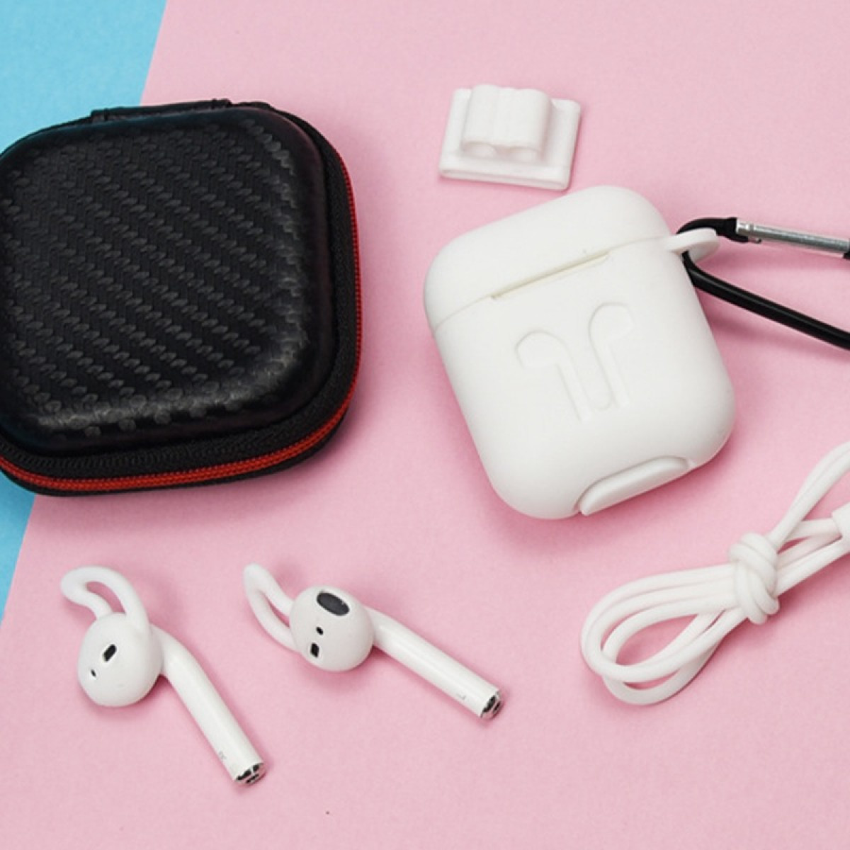 AirPods blancos, estuche, cable de carga y estuche negro dispuestos sobre una superficie rosa y azul.