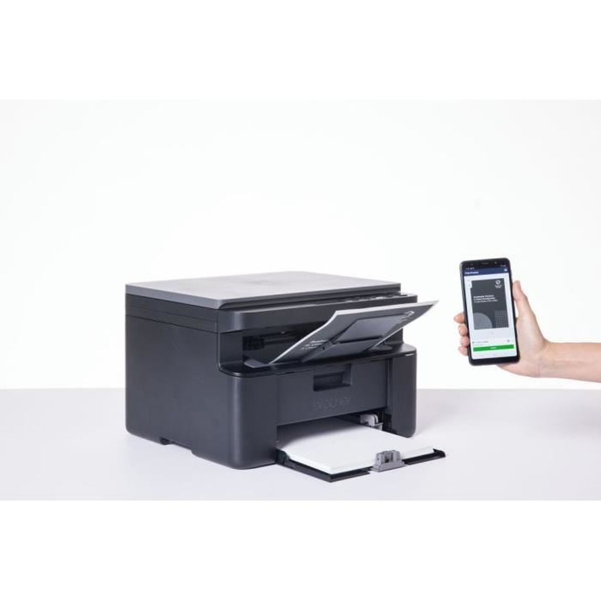 Een zwarte printer met papieruitvoer. Een hand houdt een telefoon vast met een app. Witte achtergrond.