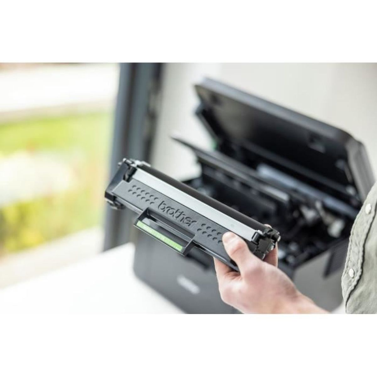 Een persoon die een Brother tonercartridge vasthoudt. De cartridge is zwart met de merknaam. Op de achtergrond staat een printer.