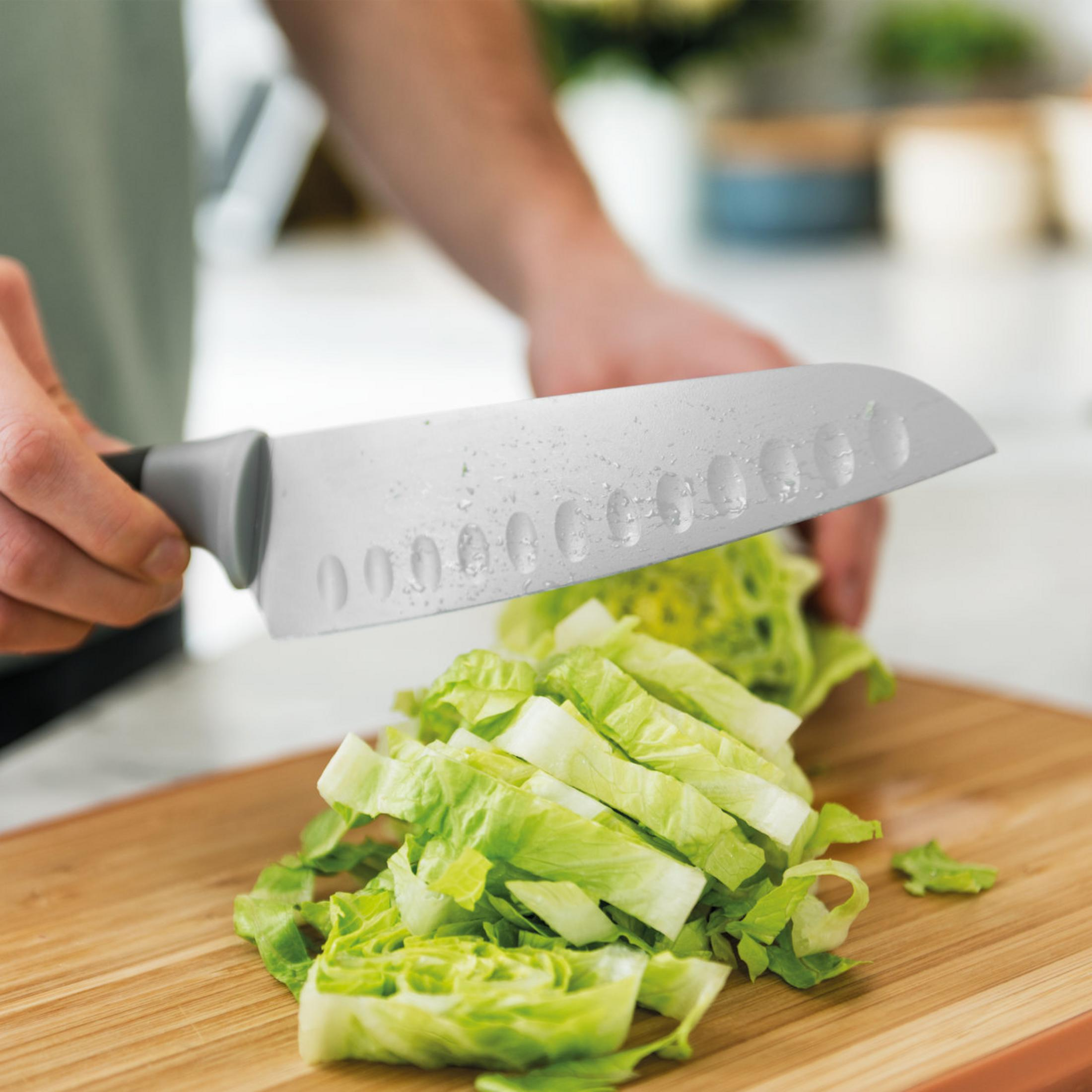 A person is cutting lettuce with a gray knife on a wooden cutting board. Chopped lettuce is in front.