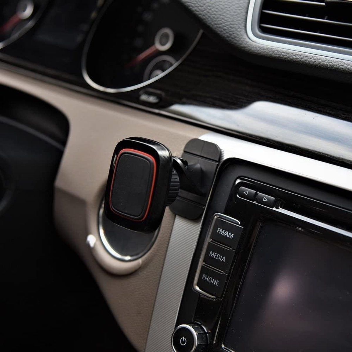 Een auto-interieur toont een telefoonhouder. De houder is zwart en rood, bevestigd aan het dashboard. Radio en snelheidsmeter zichtbaar.