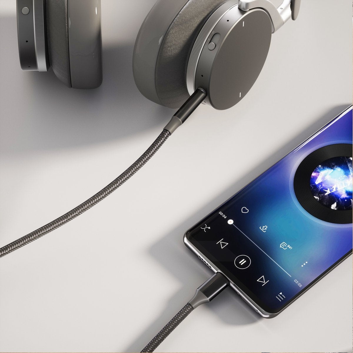 Hoofdtelefoon aangesloten op een telefoon die muziek afspeelt. Grijze kabel, zwarte telefoon, hoofdtelefoon op wit oppervlak.