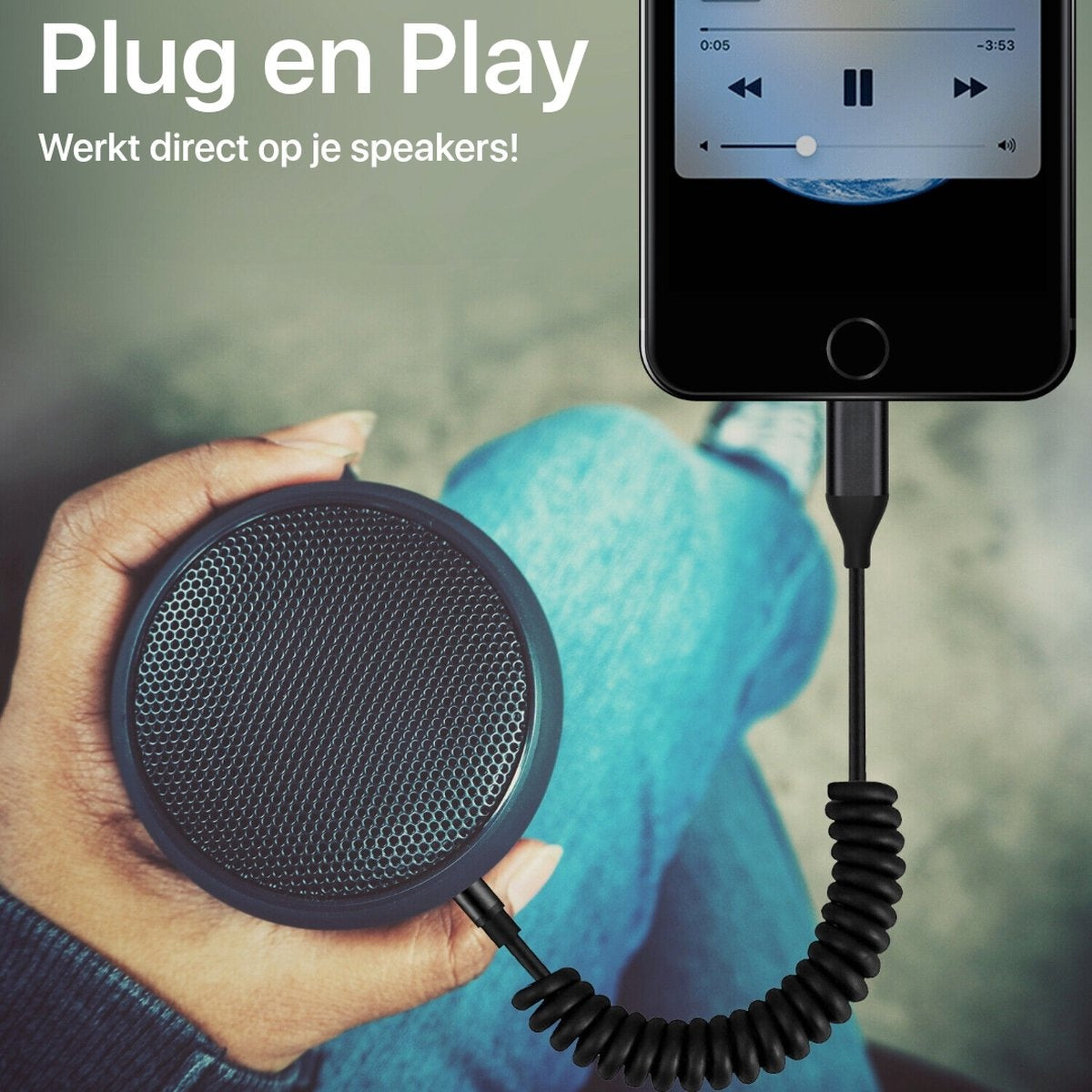 Een persoon houdt een zwarte luidspreker vast die via een zwarte kabel is aangesloten op een telefoon. Tekst zegt Plug en Play. Een spijkerbroek is zichtbaar.