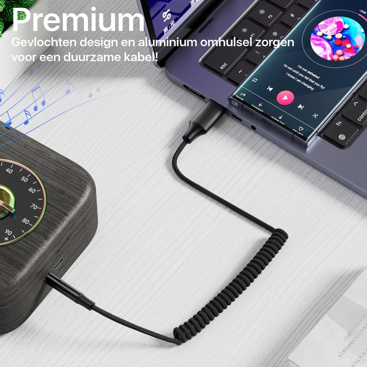 Een telefoon verbonden met een laptop en een luidspreker via een zwarte kabel. De telefoon toont een muziek-app.