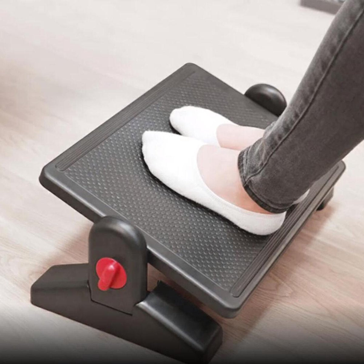 Person's feet in white socks resting on a black footrest. Gray jeans are visible. The footrest has a red adjustment knob.