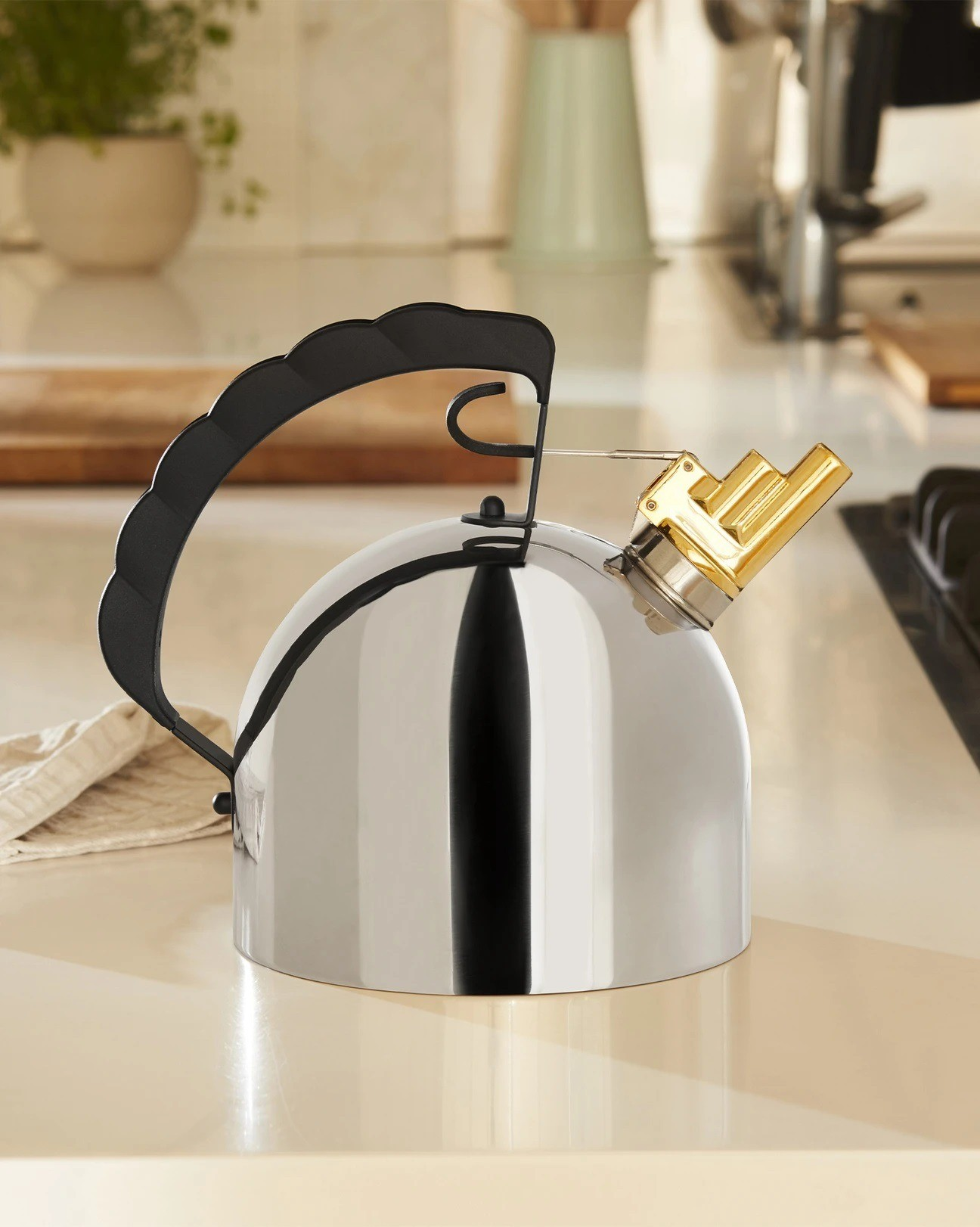 Un bollitore in acciaio inossidabile con manico nero e fischietto dorato su un piano di lavoro bianco. Sfondo della cucina.