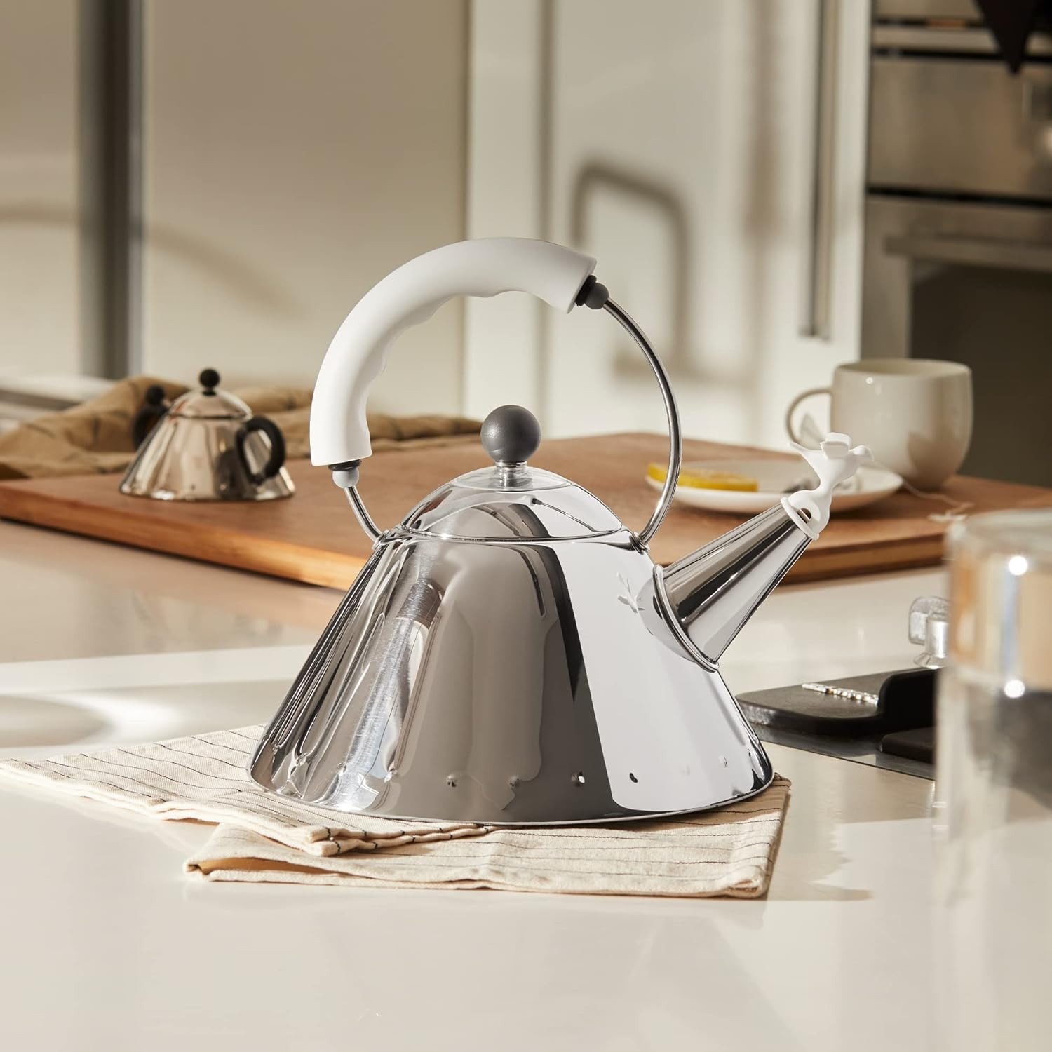 Un bollitore lucido su un piano cucina. Un secondo bollitore e una tazza sullo sfondo. Una fetta di limone su un piatto.