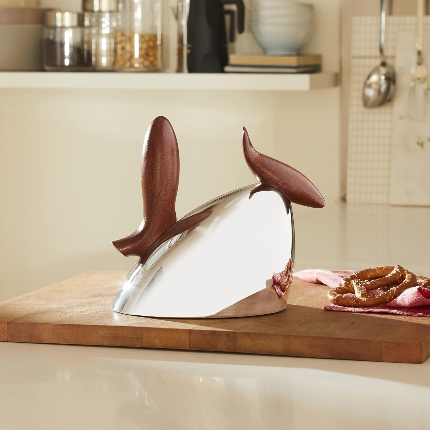 Uno strumento da cucina argentato con manici in legno su un tagliere di legno. Bretzel e un panno rosso sullo sfondo.
