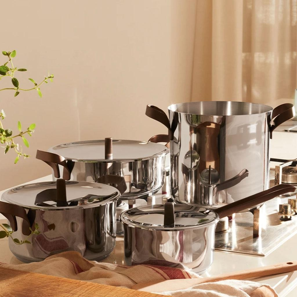 Set di pentole in acciaio inossidabile lucido su un piano della cucina. Include pentole e padelle con manici e coperchi marroni.
