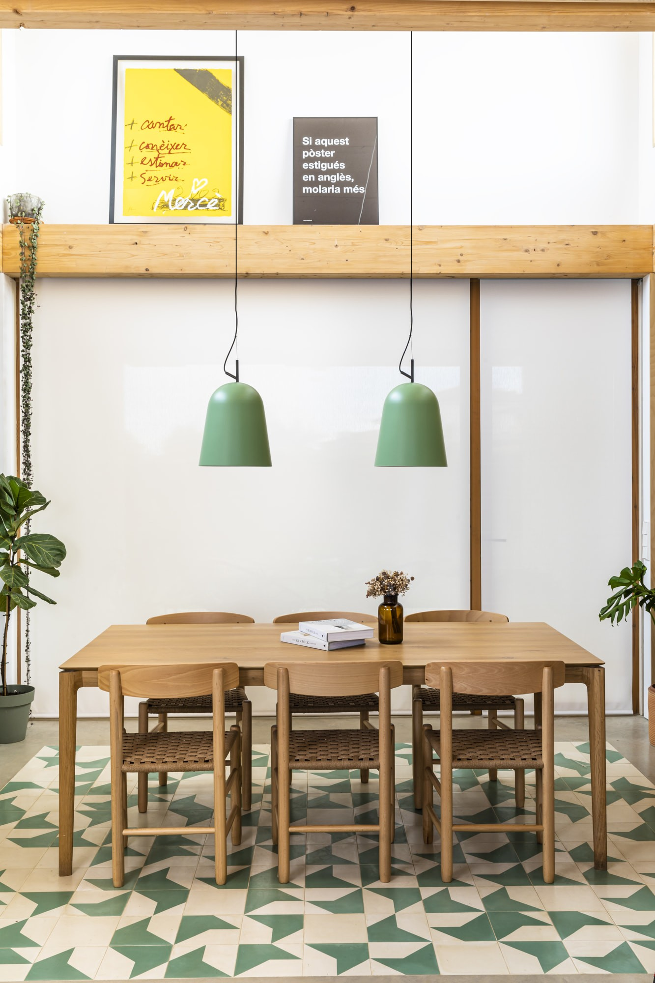 Una sala da pranzo con tavolo, sedie e lampade verdi in legno. Poster e piante sul muro. Il pavimento ha un motivo a piastrelle verdi e bianche.