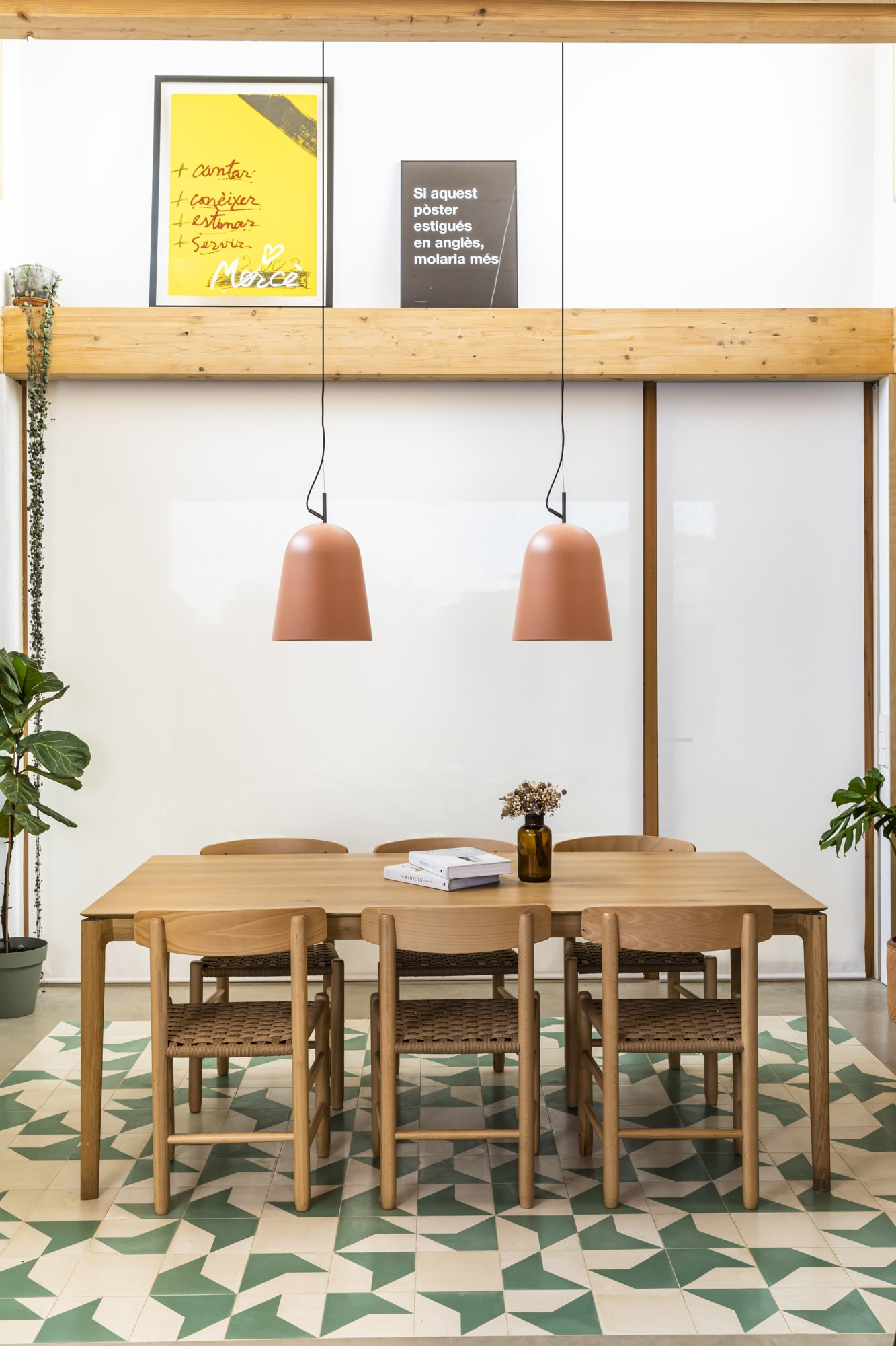 Una sala da pranzo con tavolo e sedie in legno. Due lampade a sospensione in terracotta pendono sopra. Ci sono due poster incorniciati sul muro.