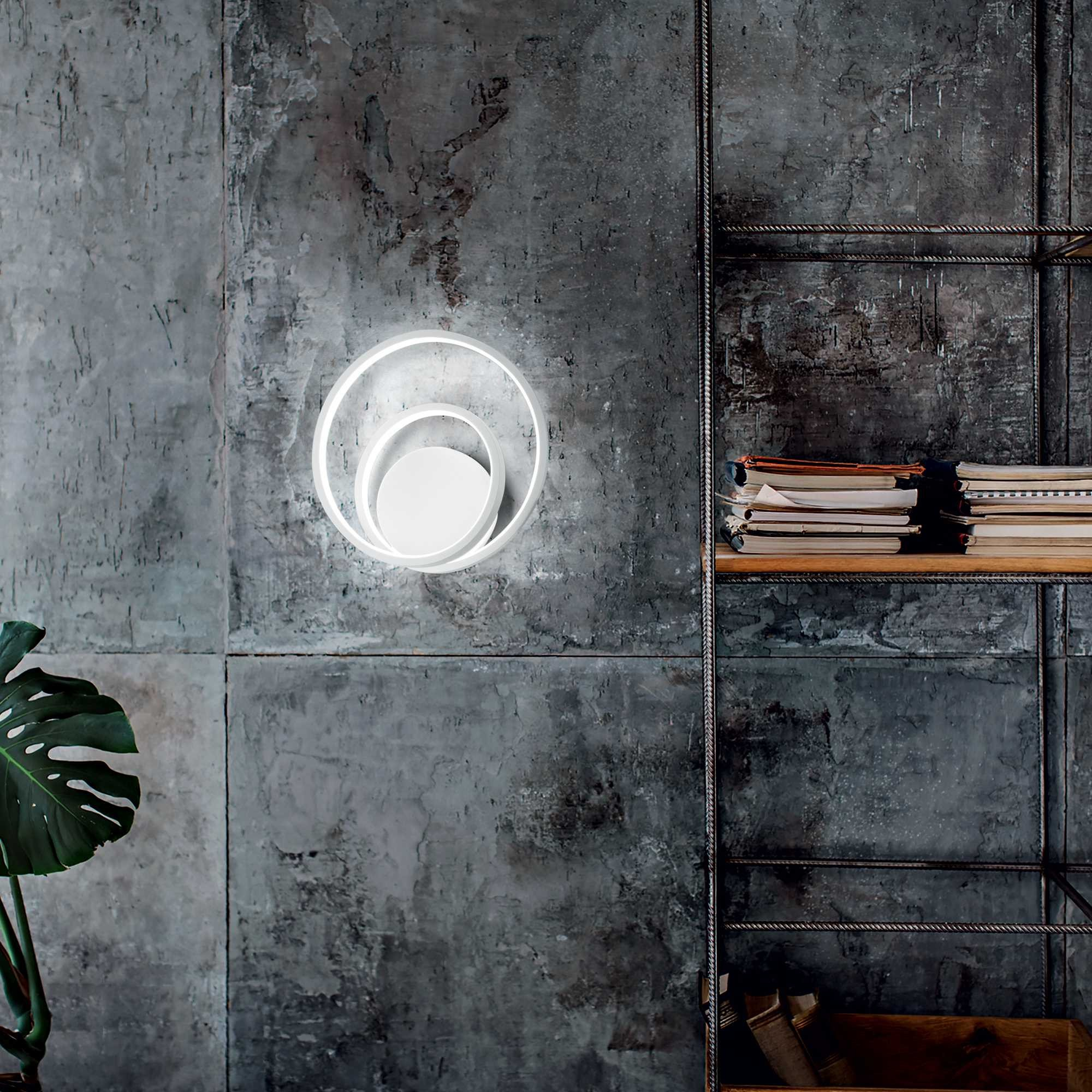 Lampada bianca moderna su muro grigio, pianta e mensola metallica con libri a destra.